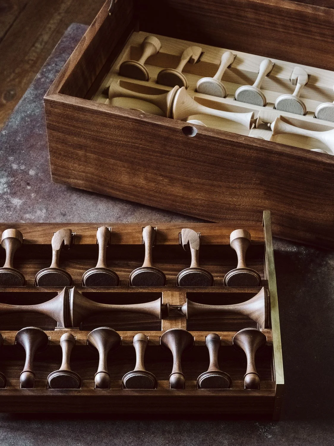 A wooden box containing multiple chess pieces with a second case of similar chess pieces nearby, all made of wood.