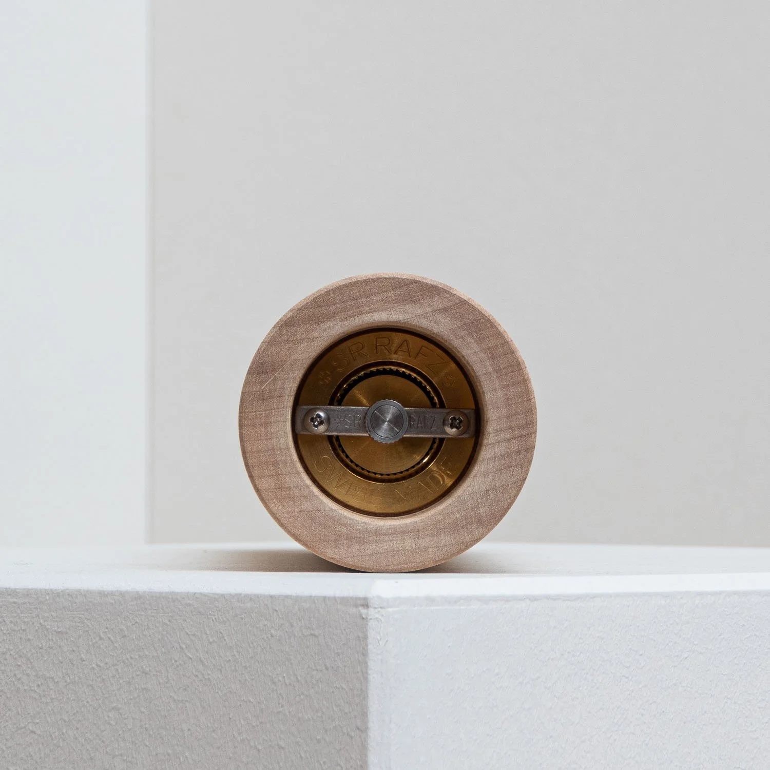 Close-up of a small brass wheel with a wooden outer ring, mounted on a white surface, with a metal screw and bolt.