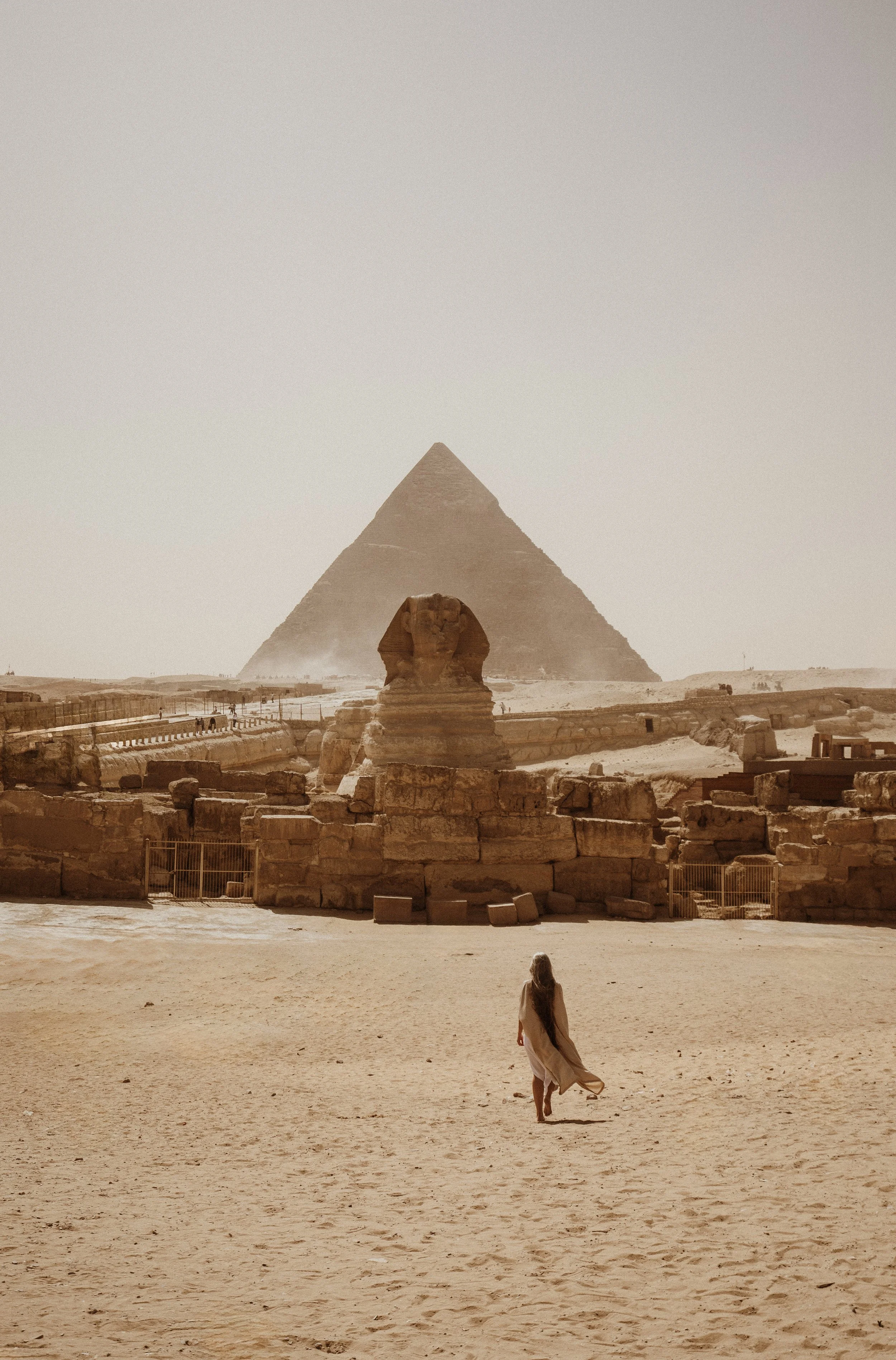 Woman walking in desert towards the Great Pyramid of Giza and the Sphinx in Egypt with other tourists in the background.