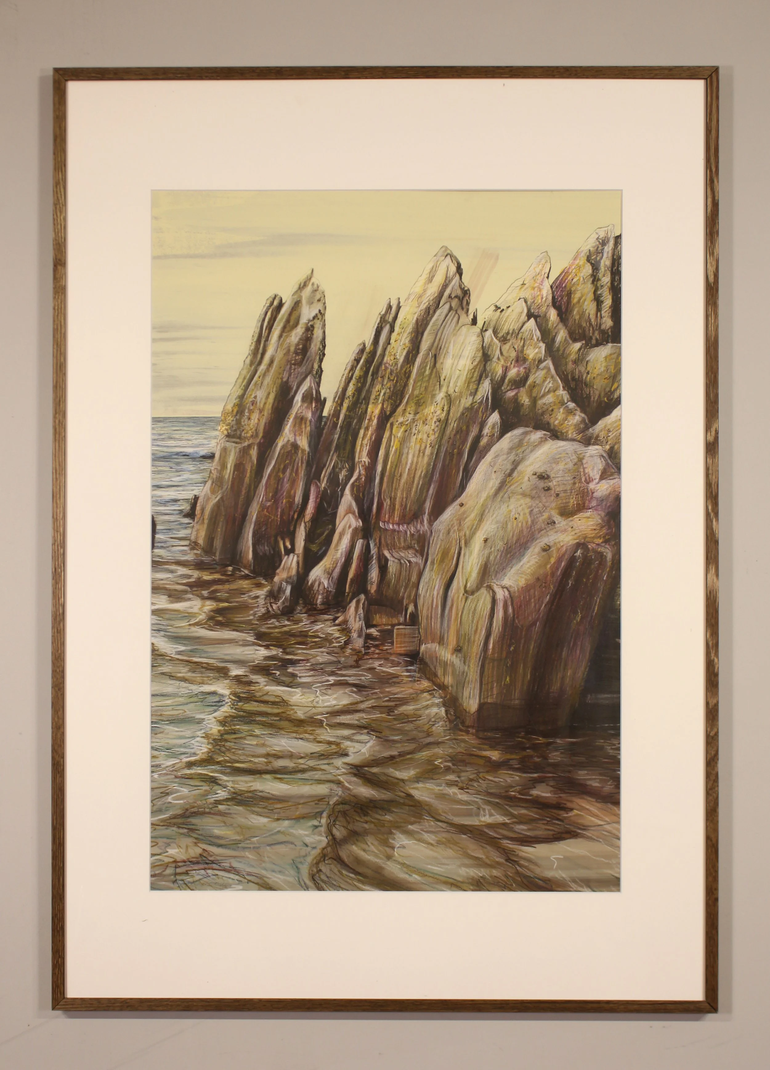 A series of jagged rocks upturned point to the yellowing sky with the approaching waves of the high tide on Freathy Beach in Whitsand Bay on the south Cornish coast. The brown hues of the reflect on the playful water seeping in.
