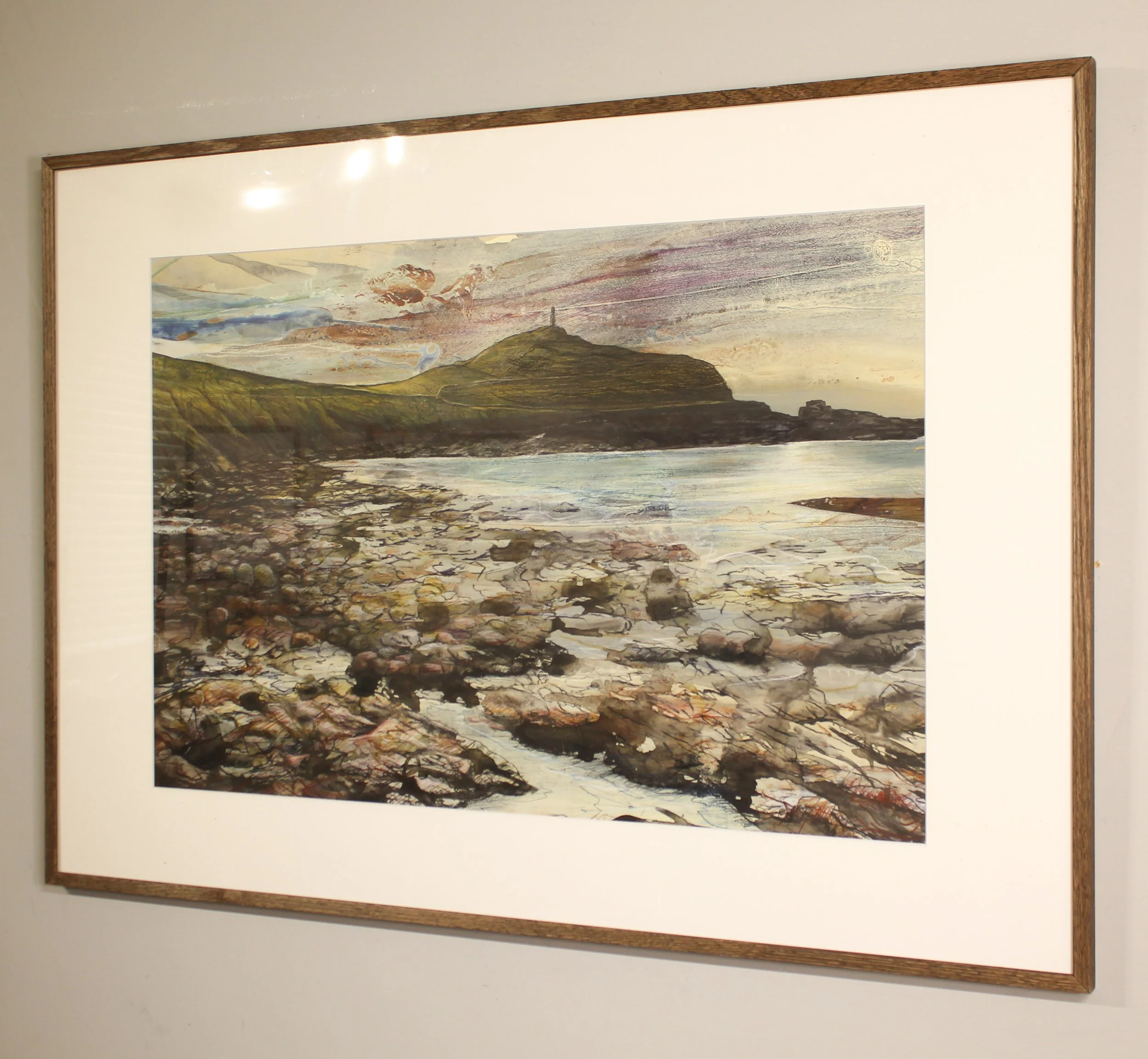 A colourful and moody drawing of a rocky beach with the Cape Cornwall headland on the horizon and a golden soft sunset behind. Expressive mark making ion the fore=ground ctreates the textures of the rocks on the sea shore.