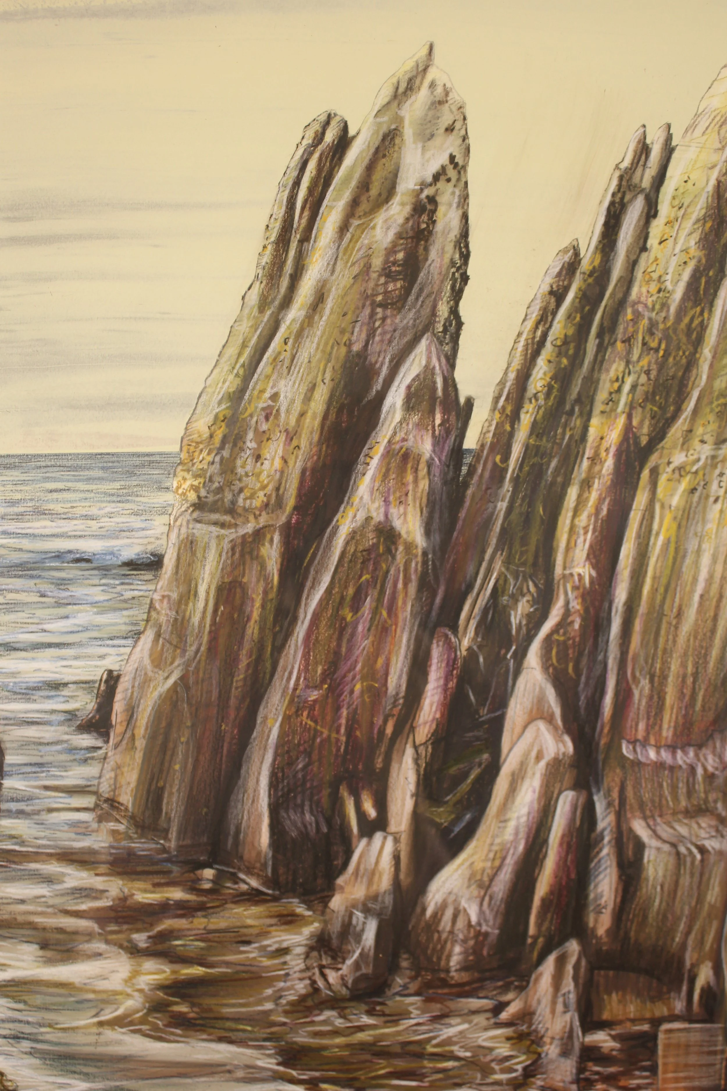 A series of jagged rocks upturned point to the yellowing sky with the approaching waves of the high tide on Freathy Beach in Whitsand Bay on the south Cornish coast. The brown hues of the reflect on the playful water seeping in.