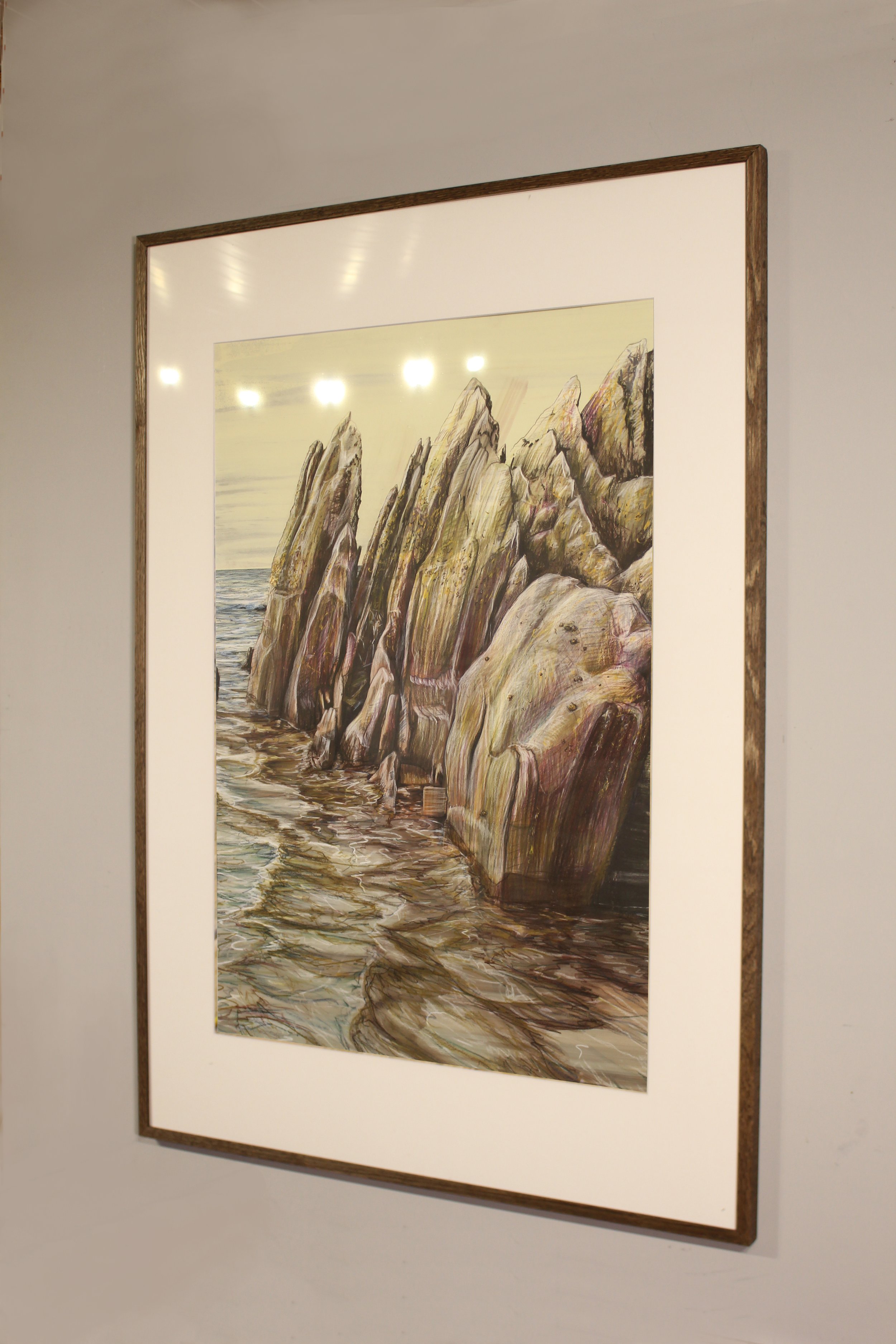 A series of jagged rocks upturned point to the yellowing sky with the approaching waves of the high tide on Freathy Beach in Whitsand Bay on the south Cornish coast. The brown hues of the reflect on the playful water seeping in.
