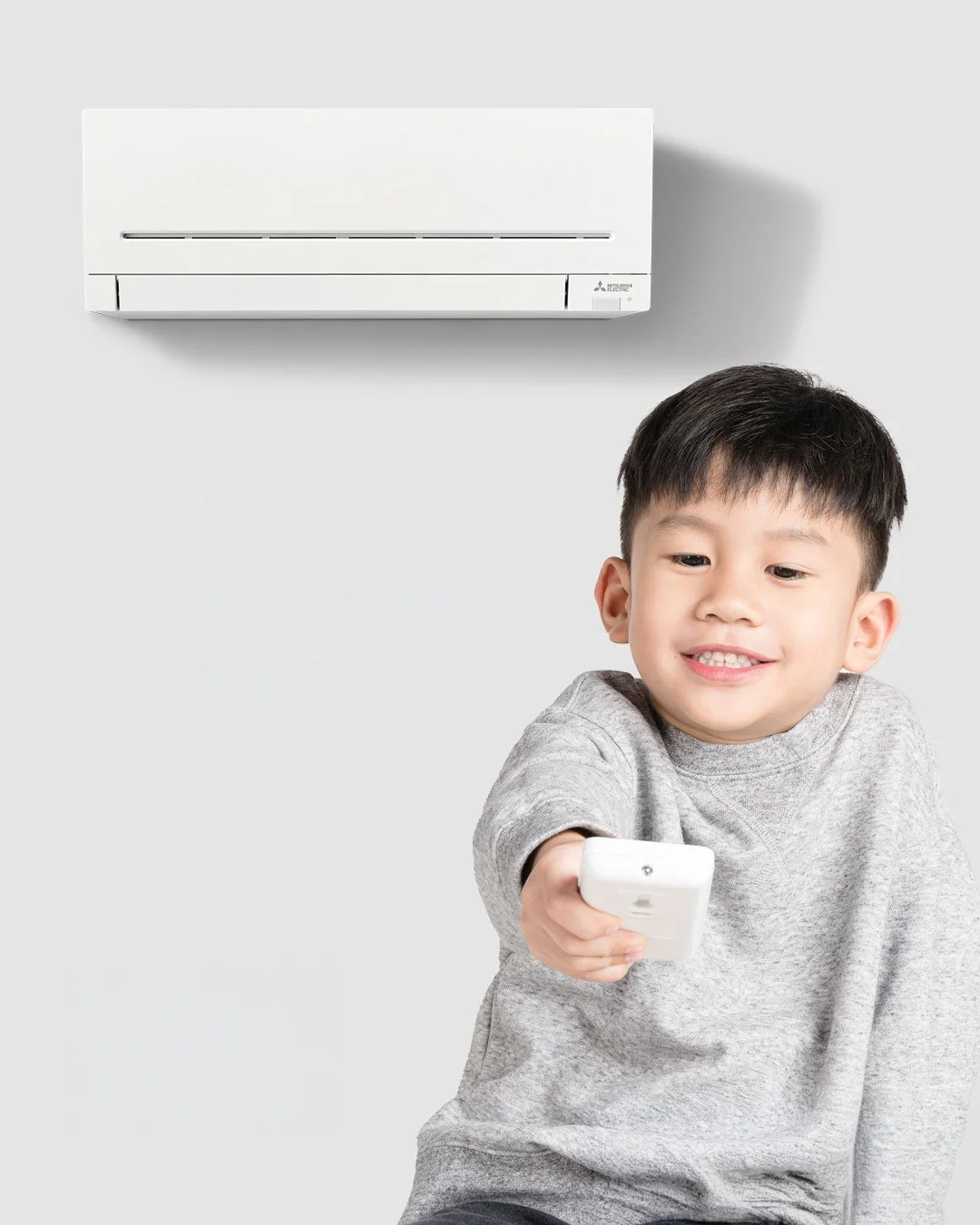 young boy in front of heat pump holding remote control