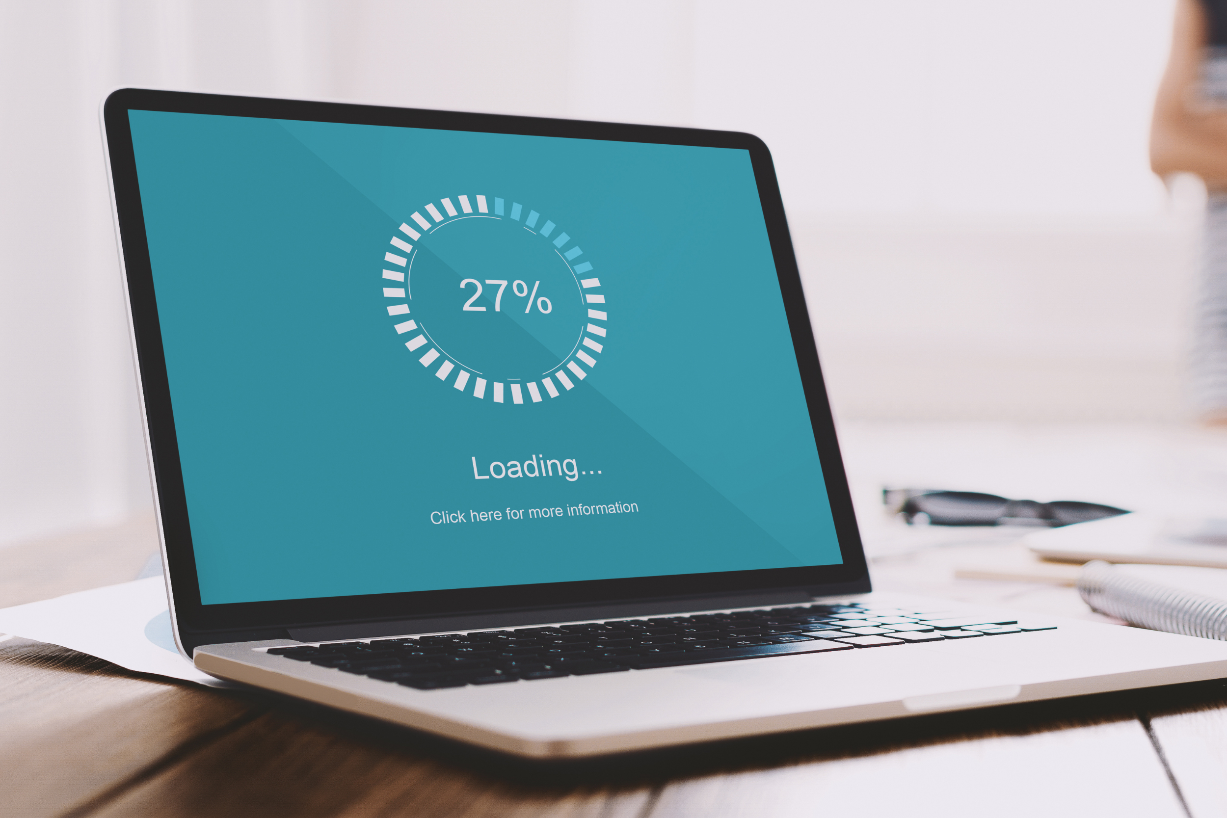 A laptop on a desk. The screen is a teal loading screen at 27% loading.