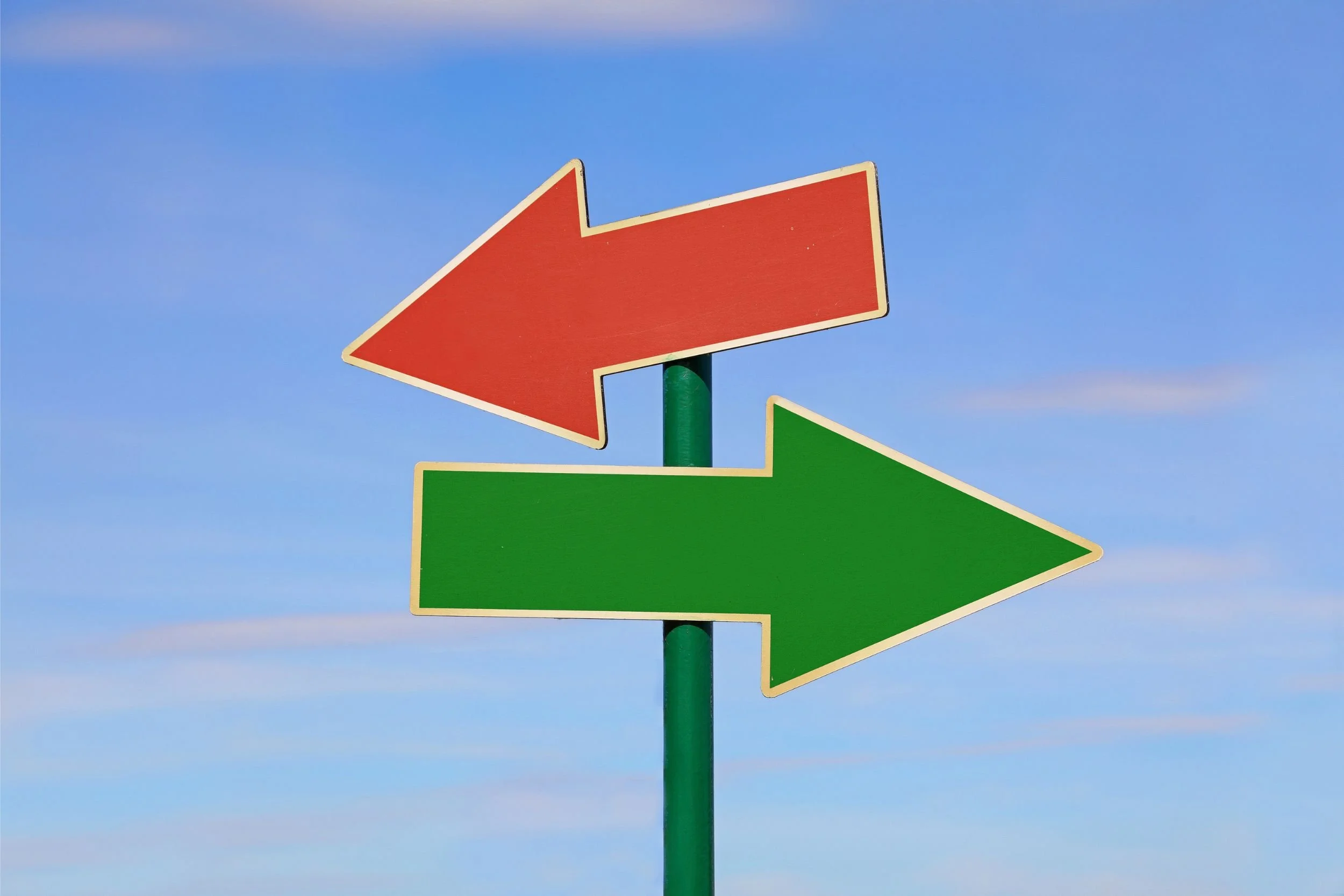 a roadsign against a blue sky with a red arrow pointing left and a green arrow pointing right, signifying two different.