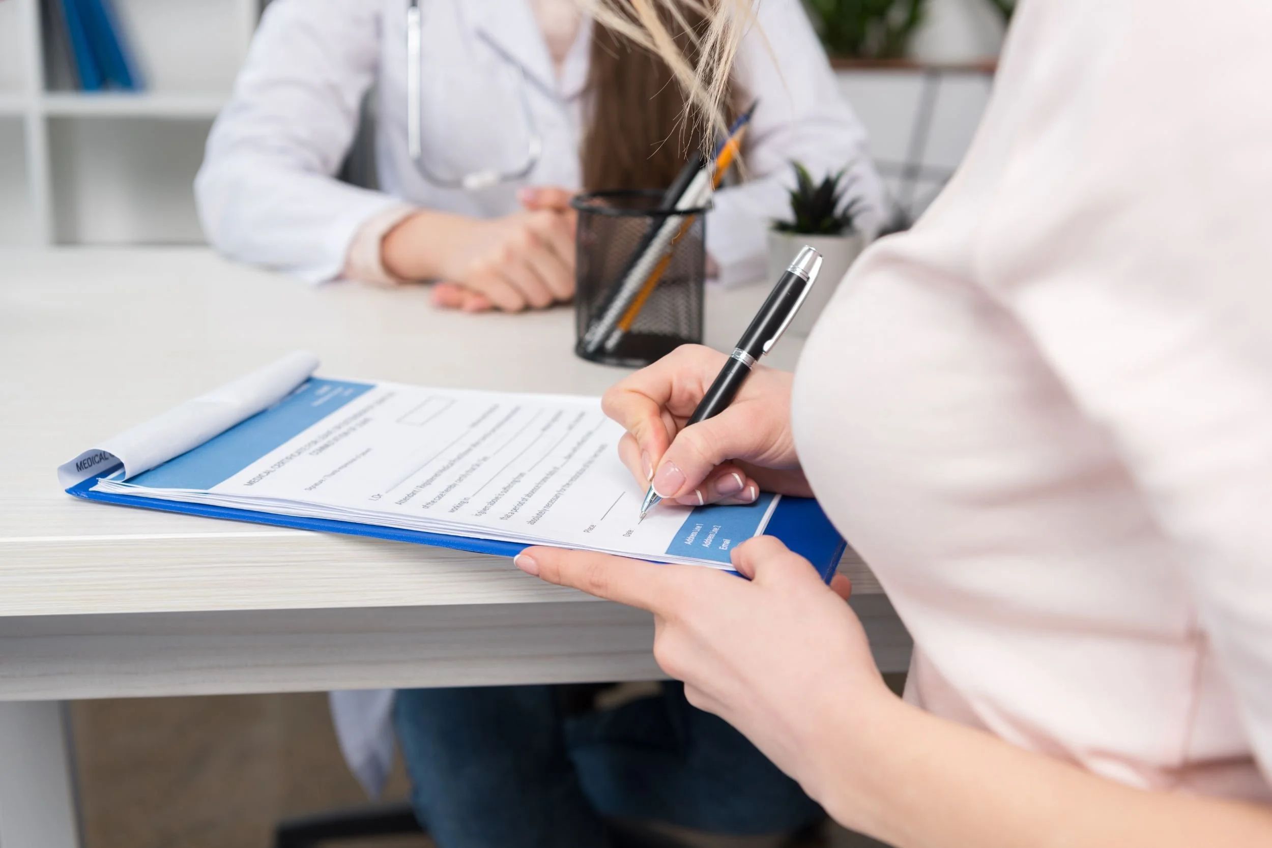 A person sitting in a clinic with a physician, filling out medical forms.