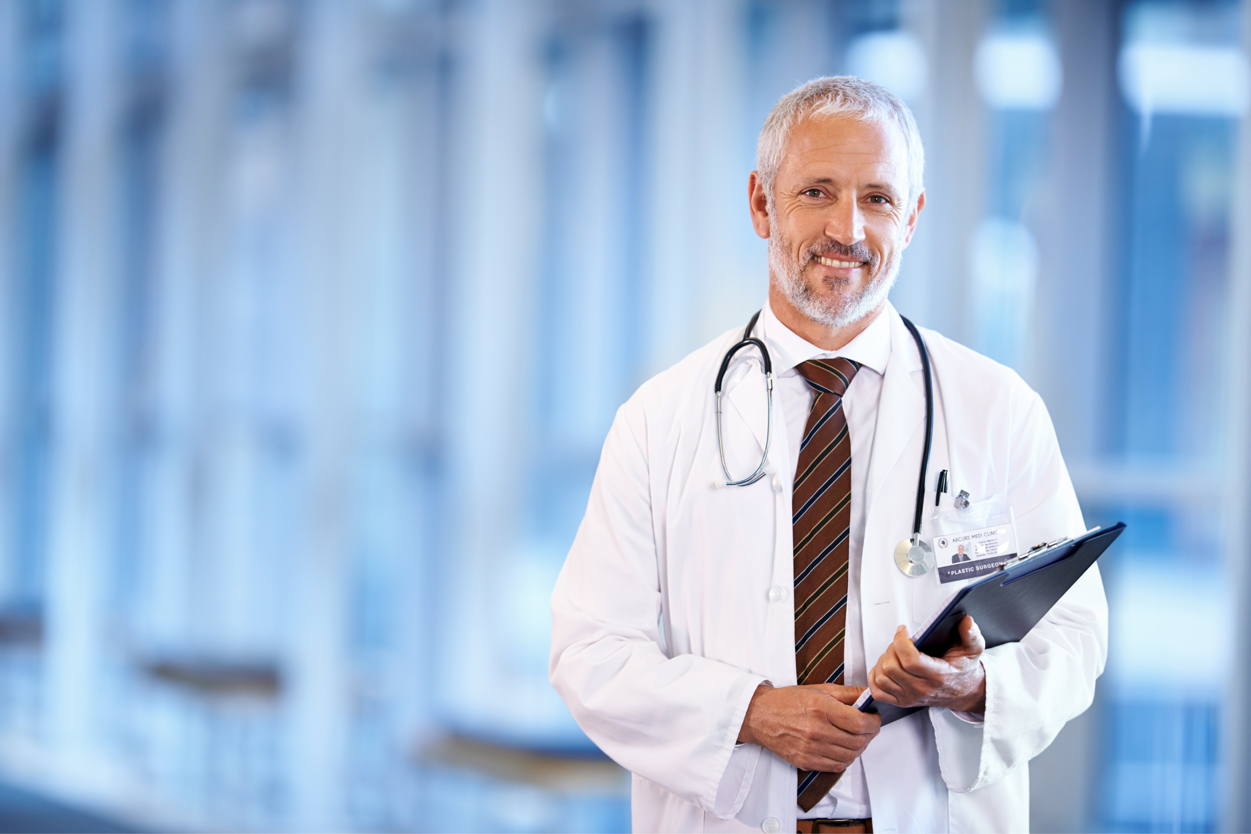 A white-haired doctor smiling and holding a clipboard.