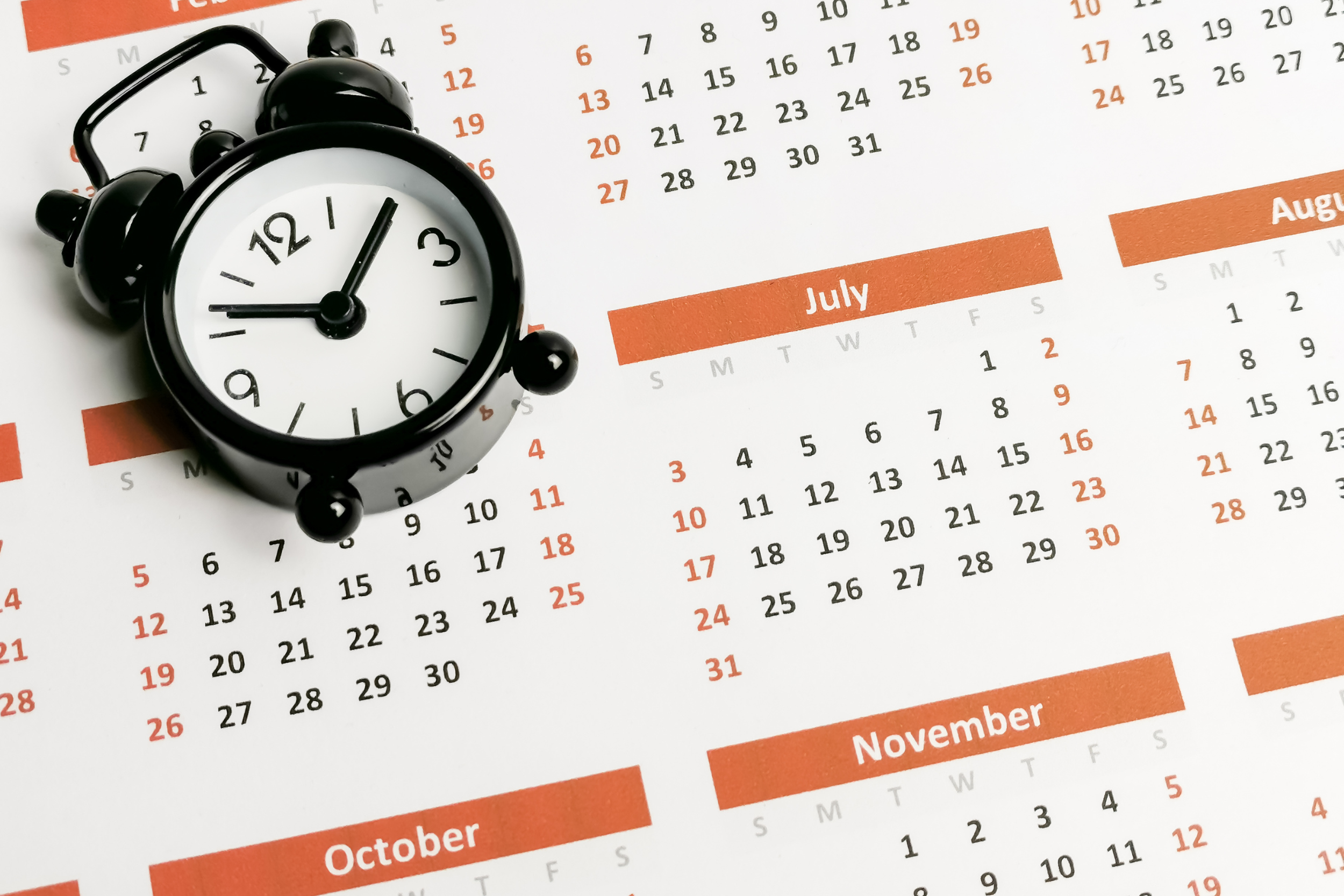 A black alarm clock laying on top of a full-year calendar.