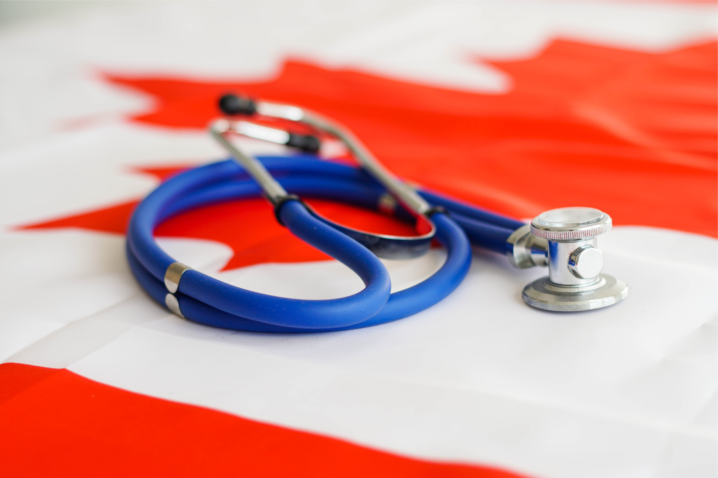 Metal stethoscope laying on a Canadian flag.