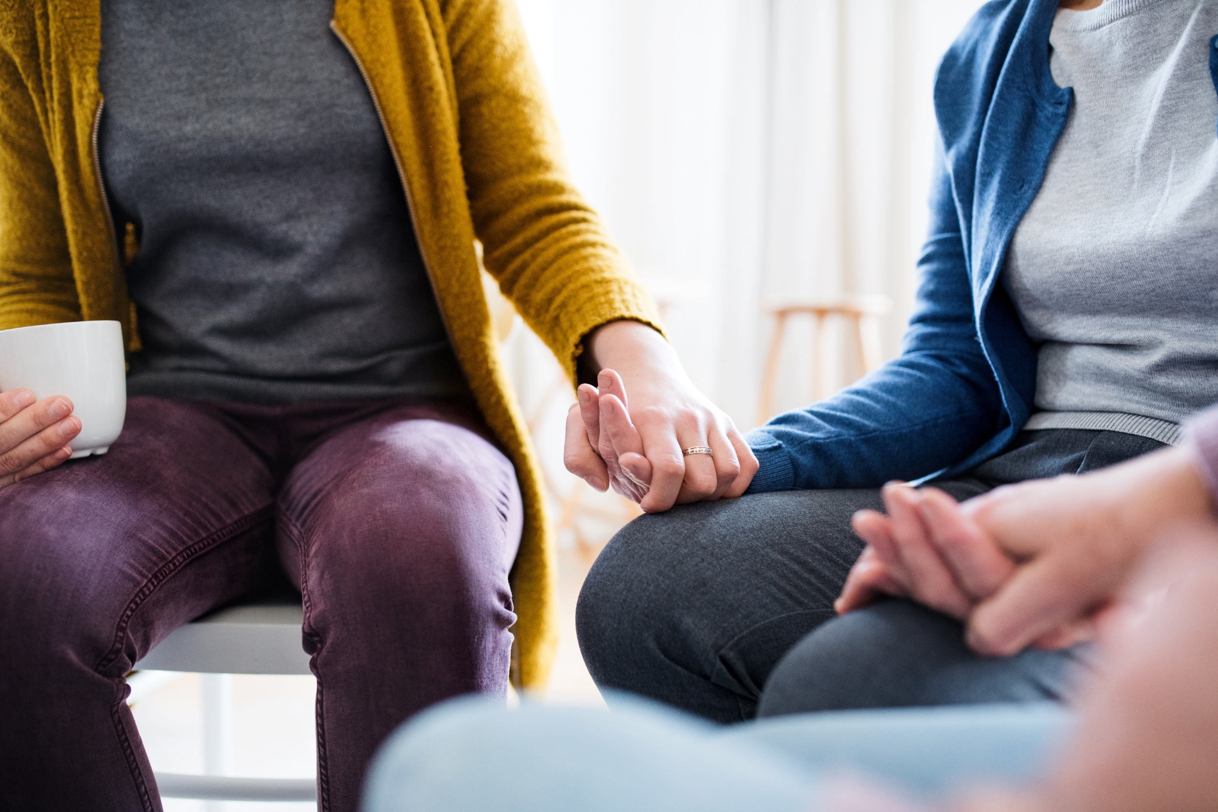 Midsection of men and women sitting in a circle during group therapy.