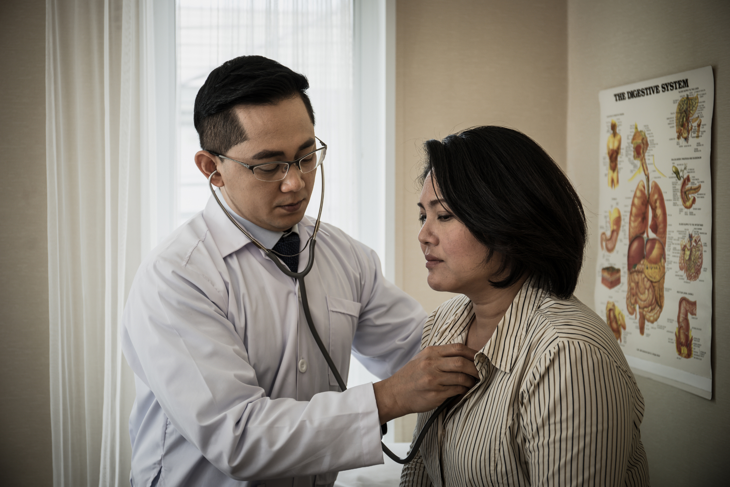 A doctor in a white coat checks a patient's heart and lungs with a stethoscope.