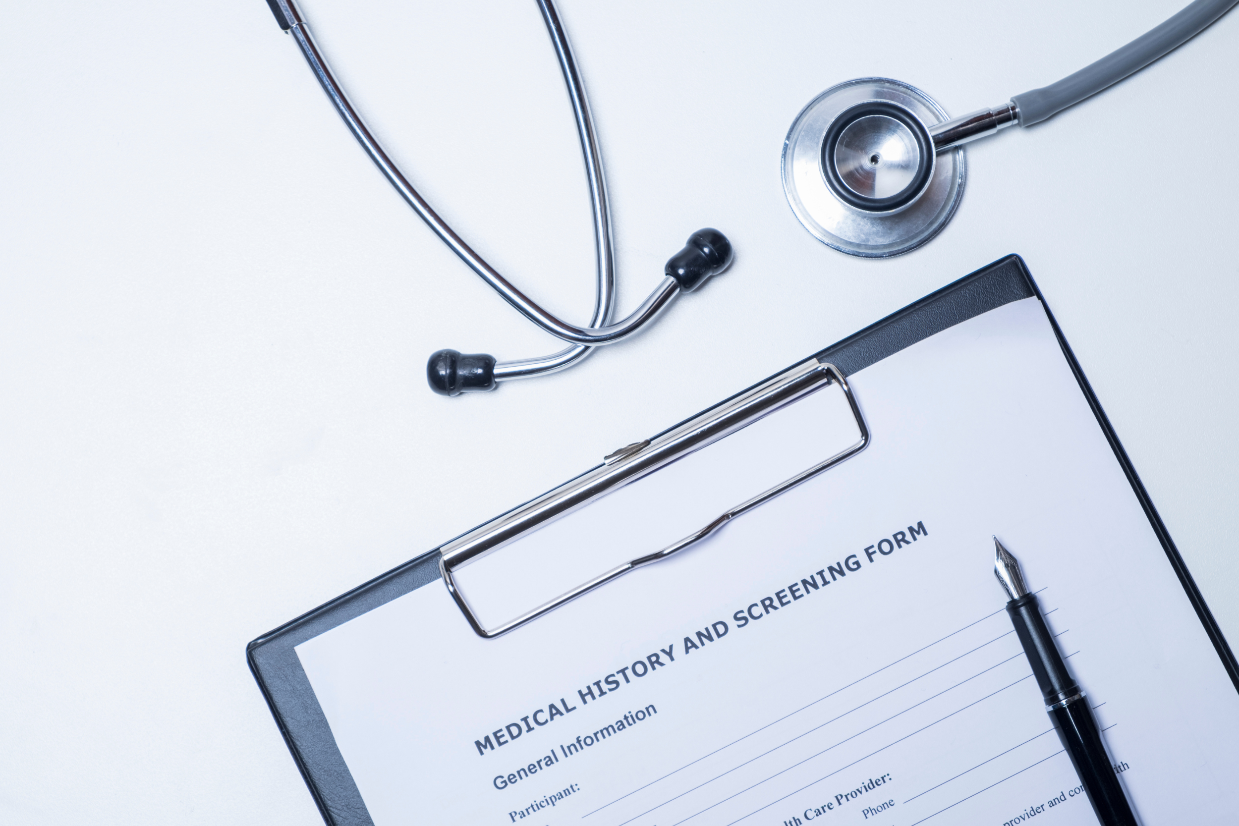 A medical history and screening form on a clipboard, surrounded by a pen and a stethoscope.