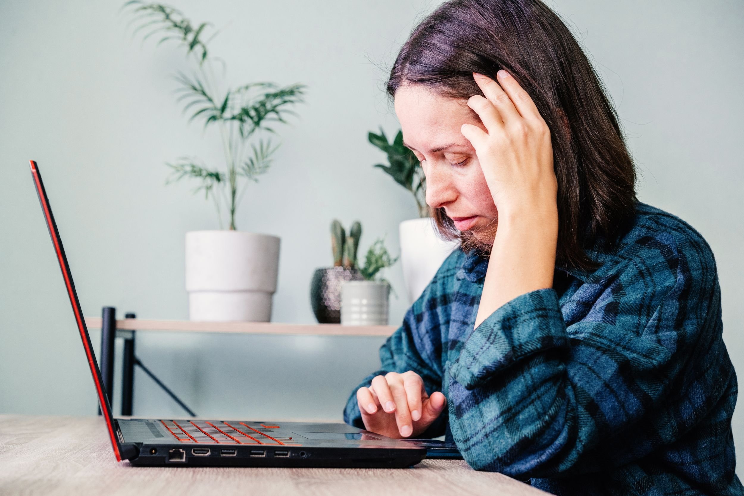 A woman sitting at a table checking for updates on her laptop, looking stressed.