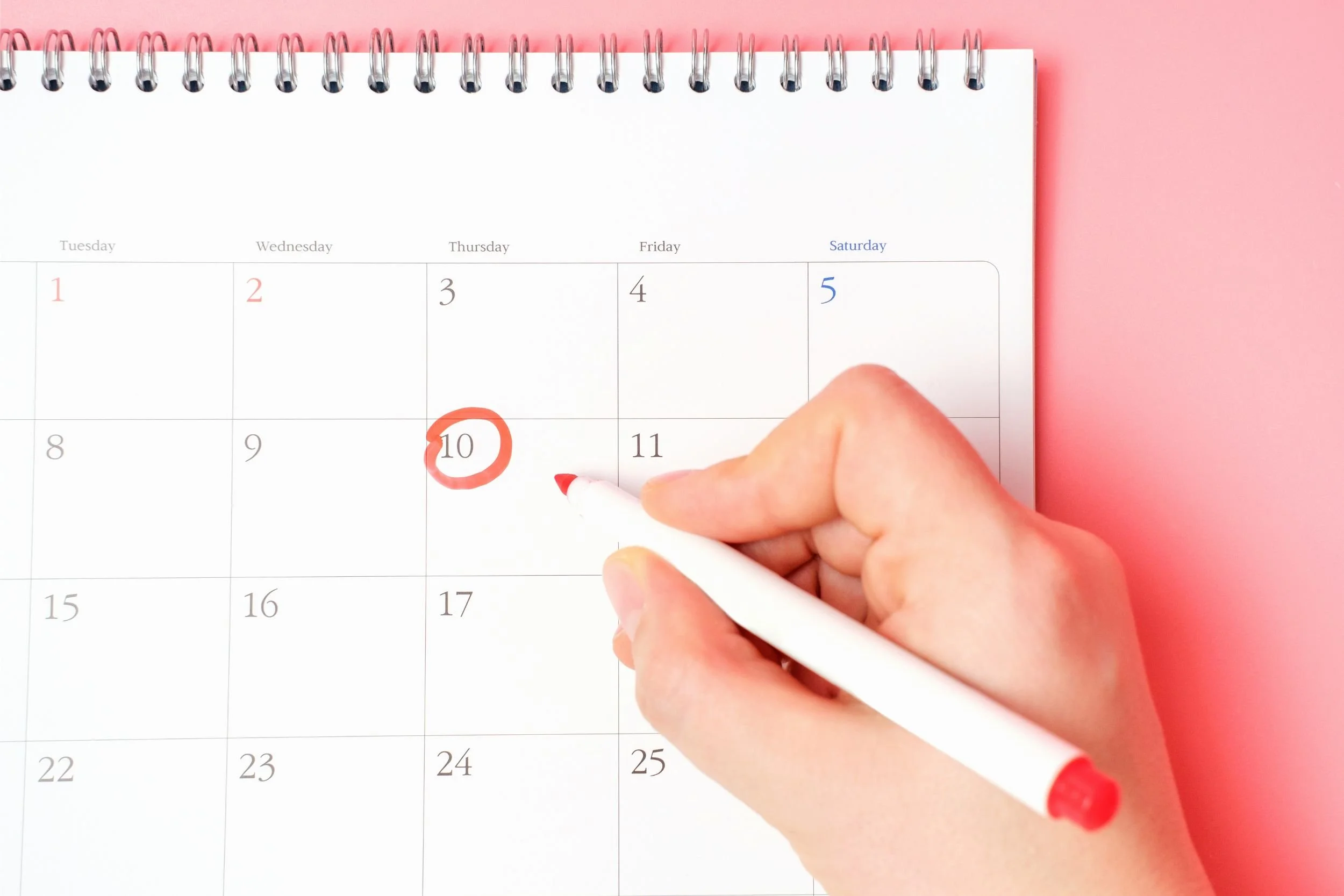 A hand holding a red marker circles a date on a white calendar.
