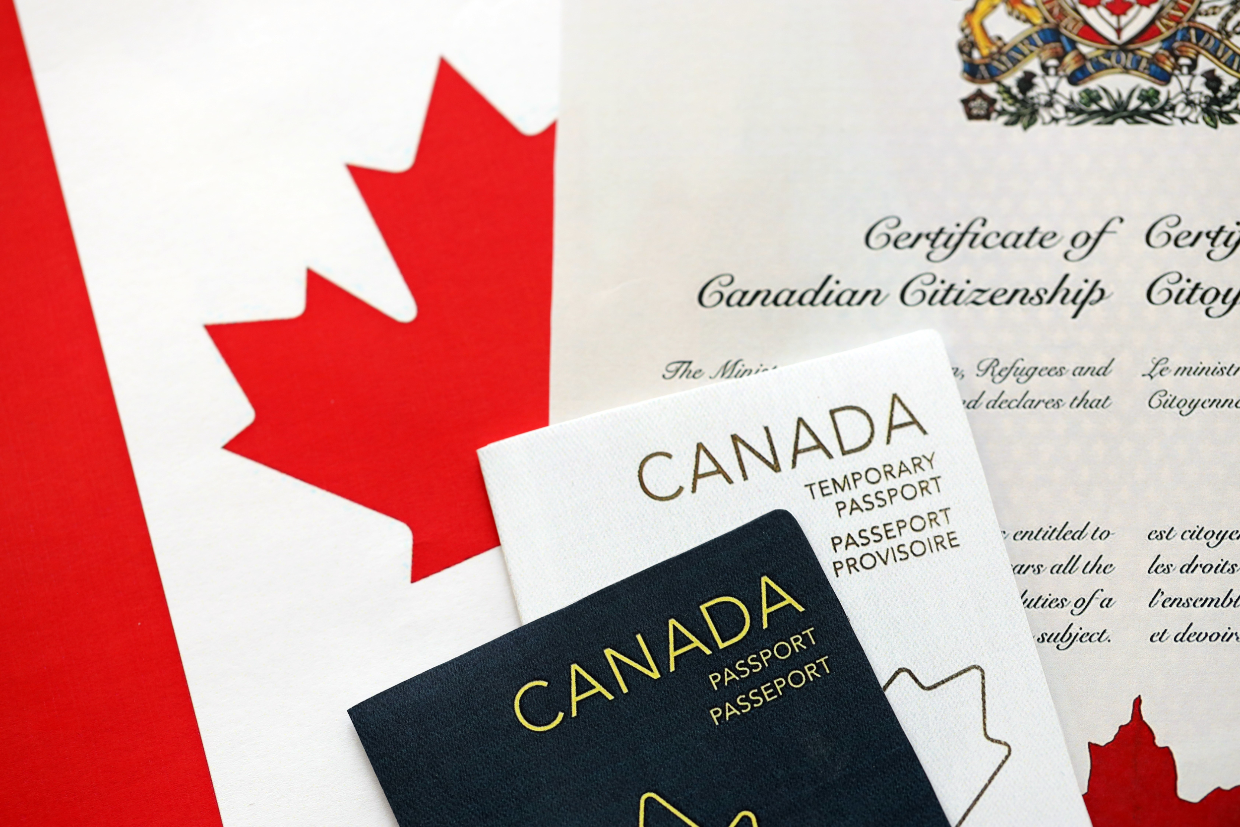 Certificate of Canadian Citizenship and a temporary Canadian passport beside a Canadian flag.
