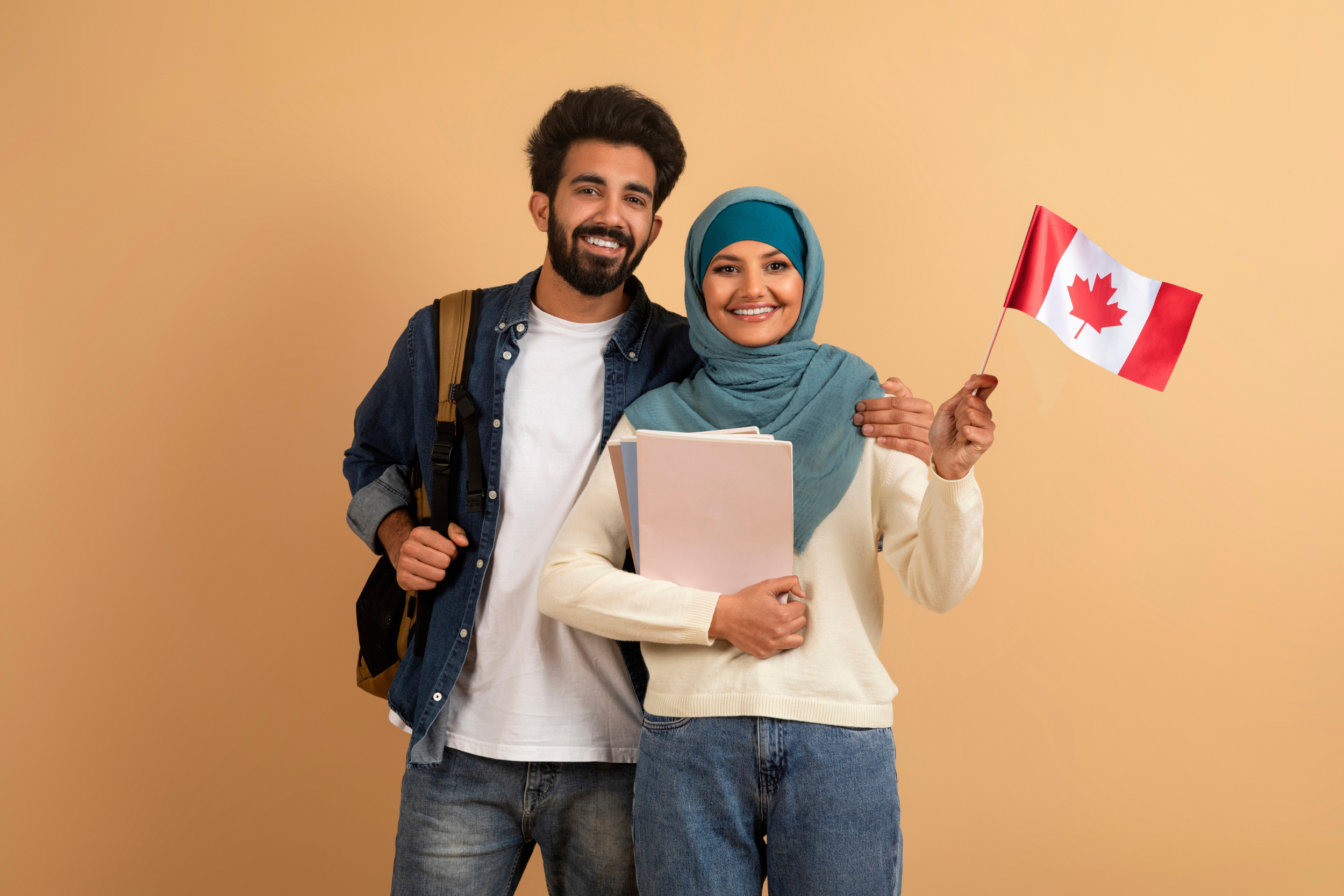 Smiling immigrant couple with canadian flag and workbooks posing on beige background