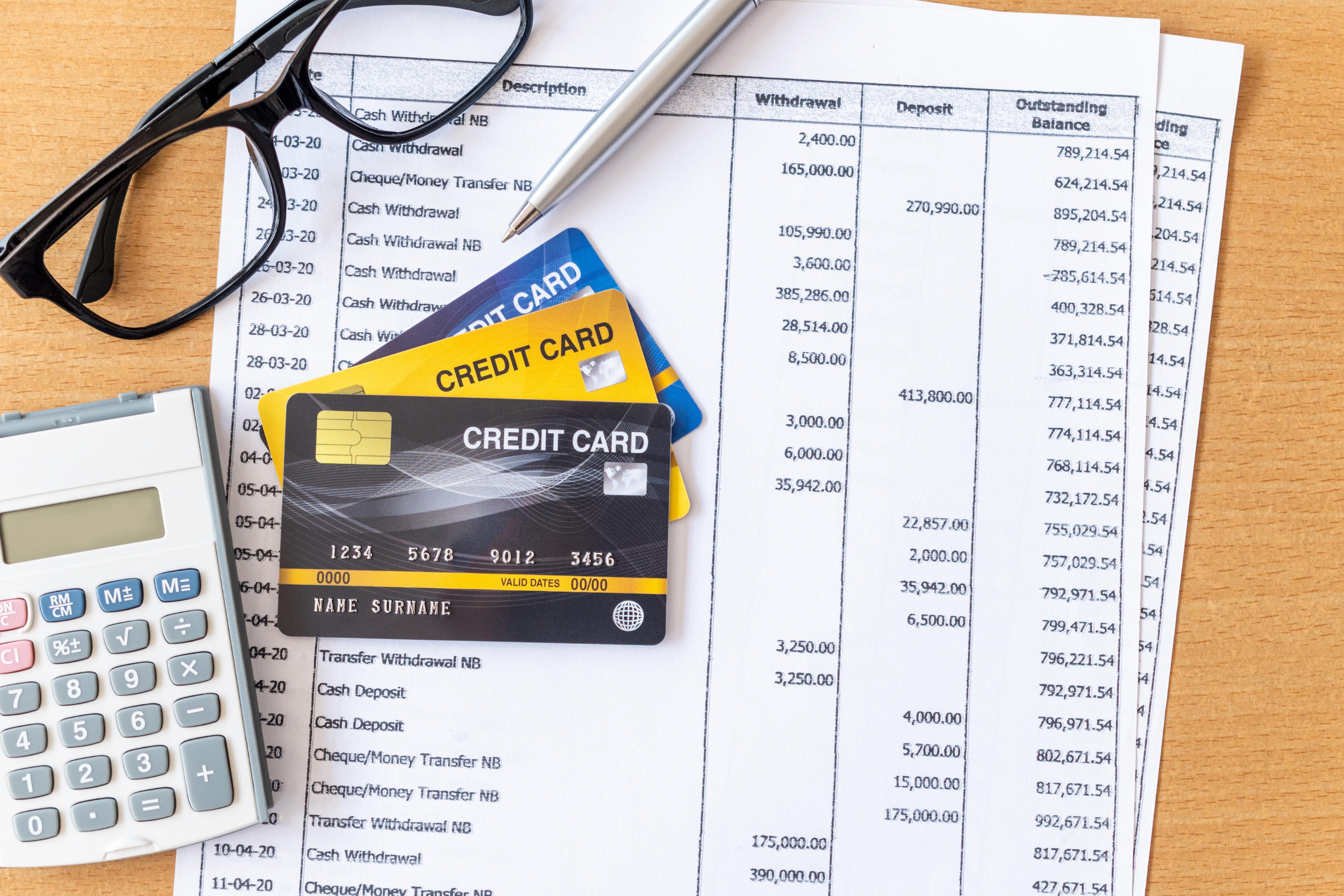 A bank statement on a desk next to a calculator and a pair of glasses, with three credit cards lying on top.