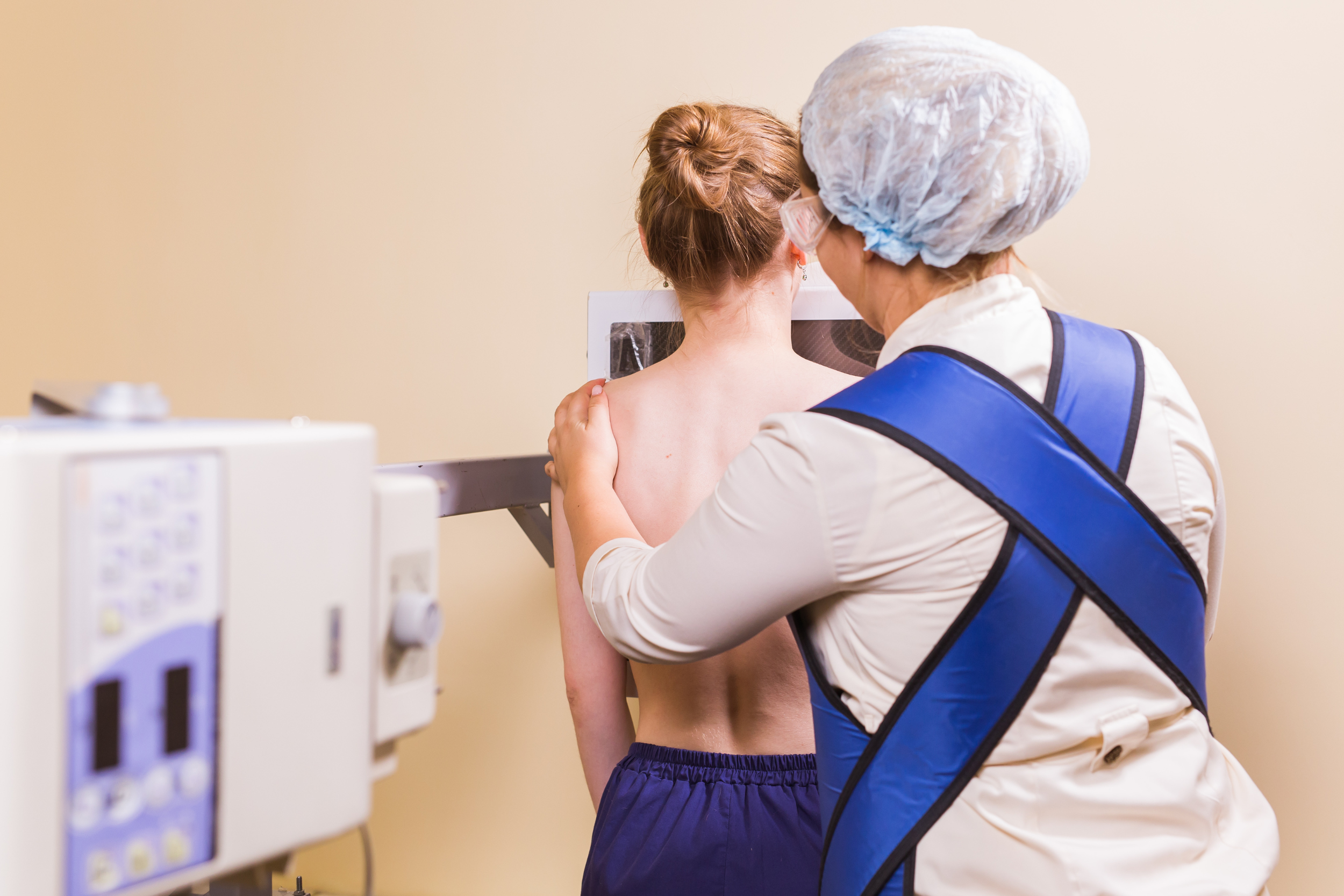 A young woman receives a chest X-ray with a medical professional beside her.