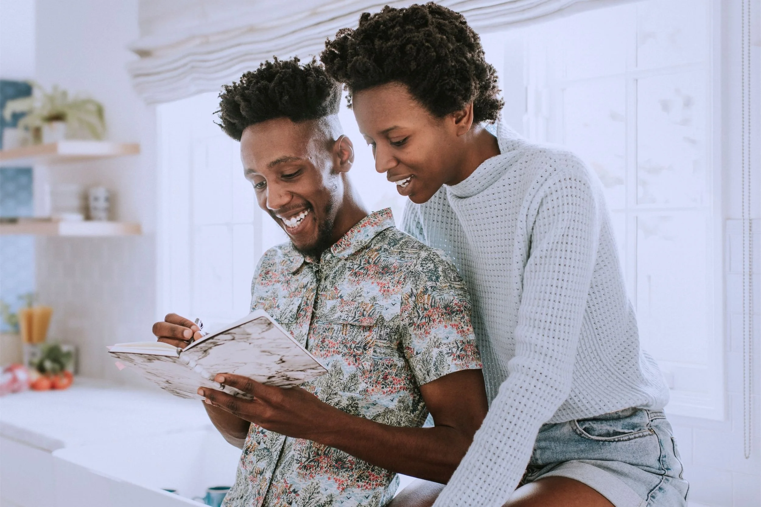 A happy couple sitting in their home, marking important information down in a planner.