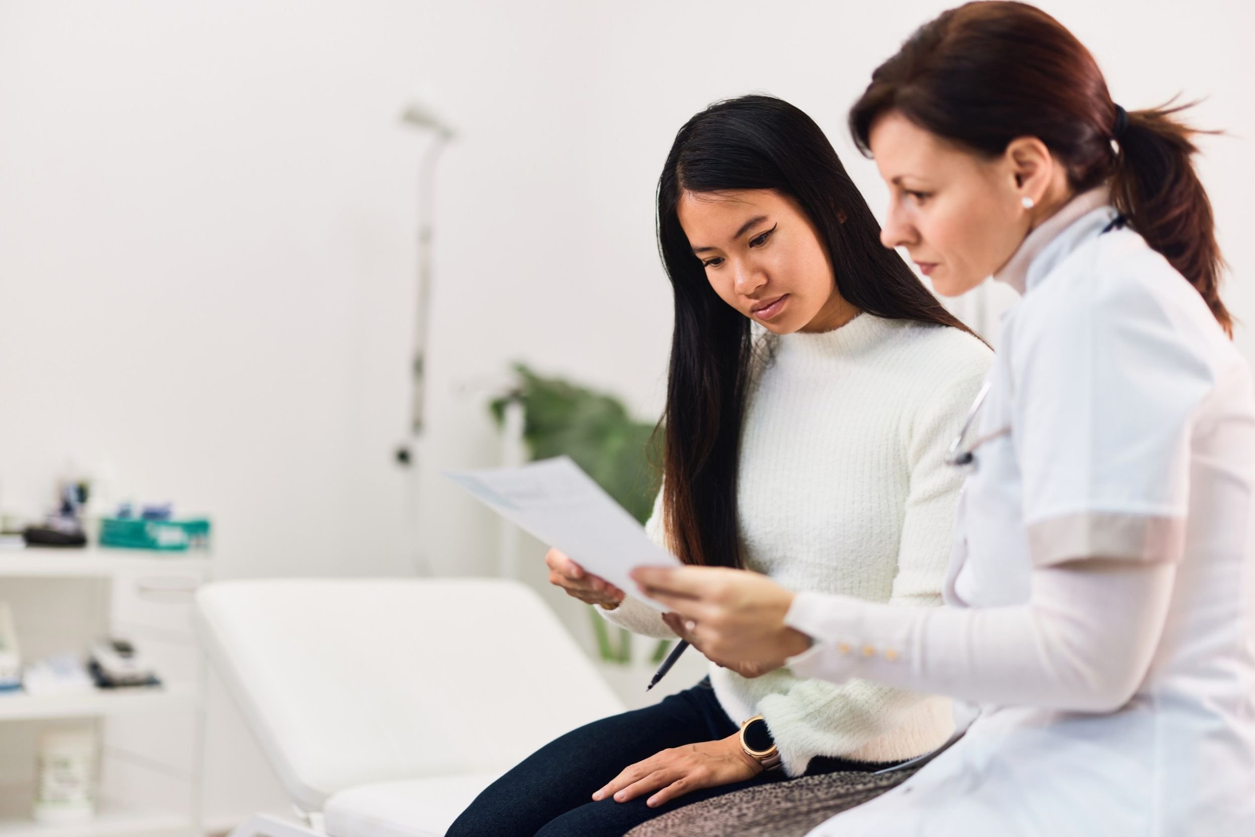 A patient sitting on a hospital bed with a doctor, reviewing test results together.