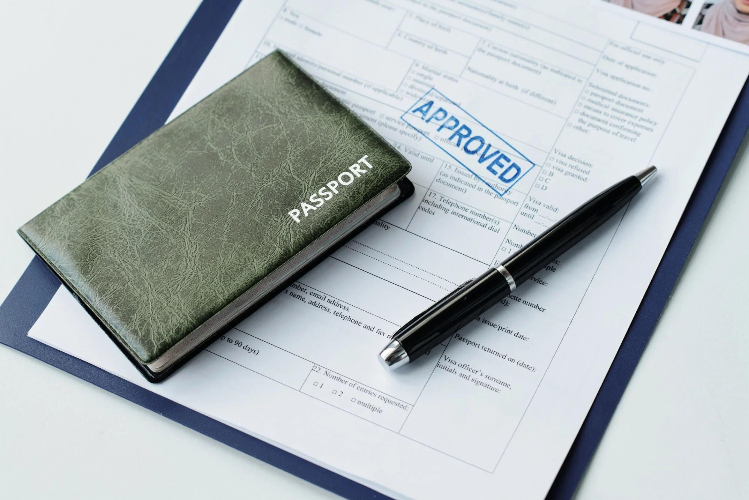 A passport holder and pen on top of an application with a blue stamp saying "Approved" on it.