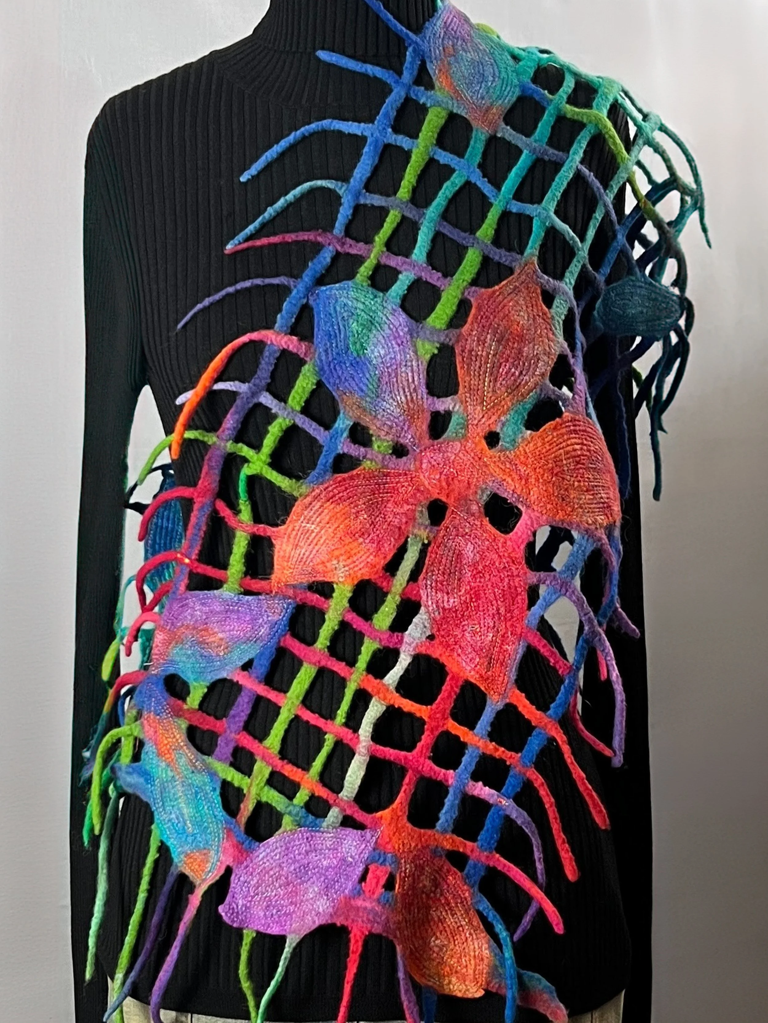 Hand felted merino wool wrap in a blend of warm and cool colors, featuring an airy lattice design with sculptural floral accents. 