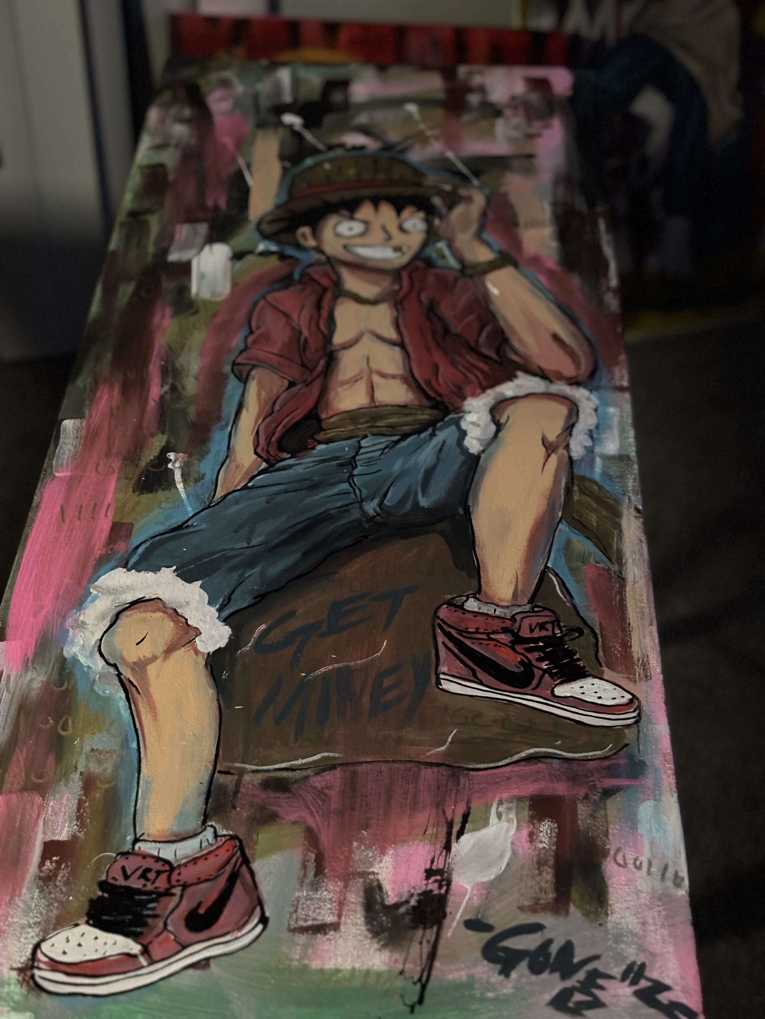 Colorful illustration of a happy cartoon boy with black hair, wearing a large wide-brimmed hat, red jacket, and denim shorts. He is sitting with one arm resting on his head, smiling broadly.