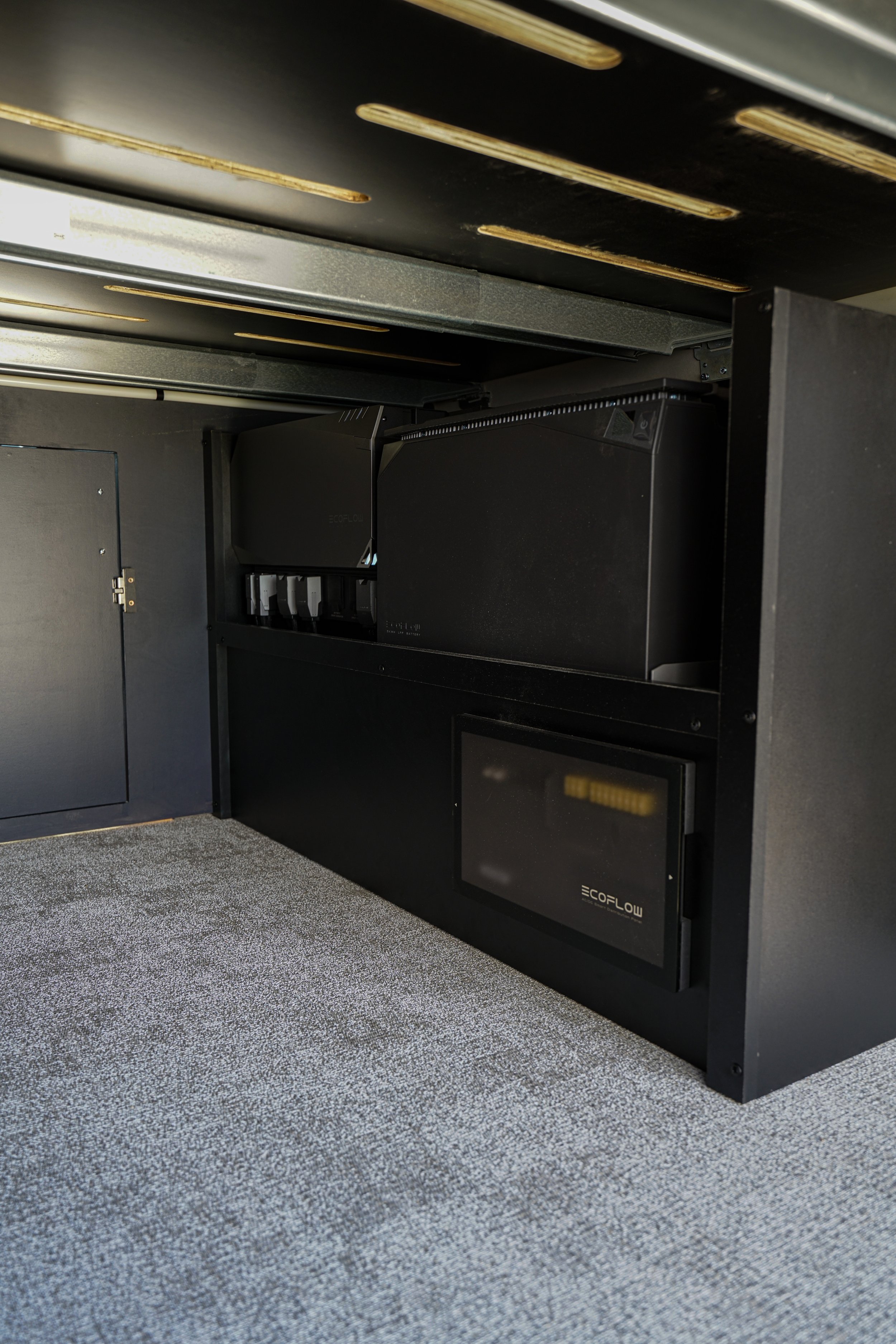 Cabinet with electronic components, including EcoFlow power station, on a gray carpeted floor.