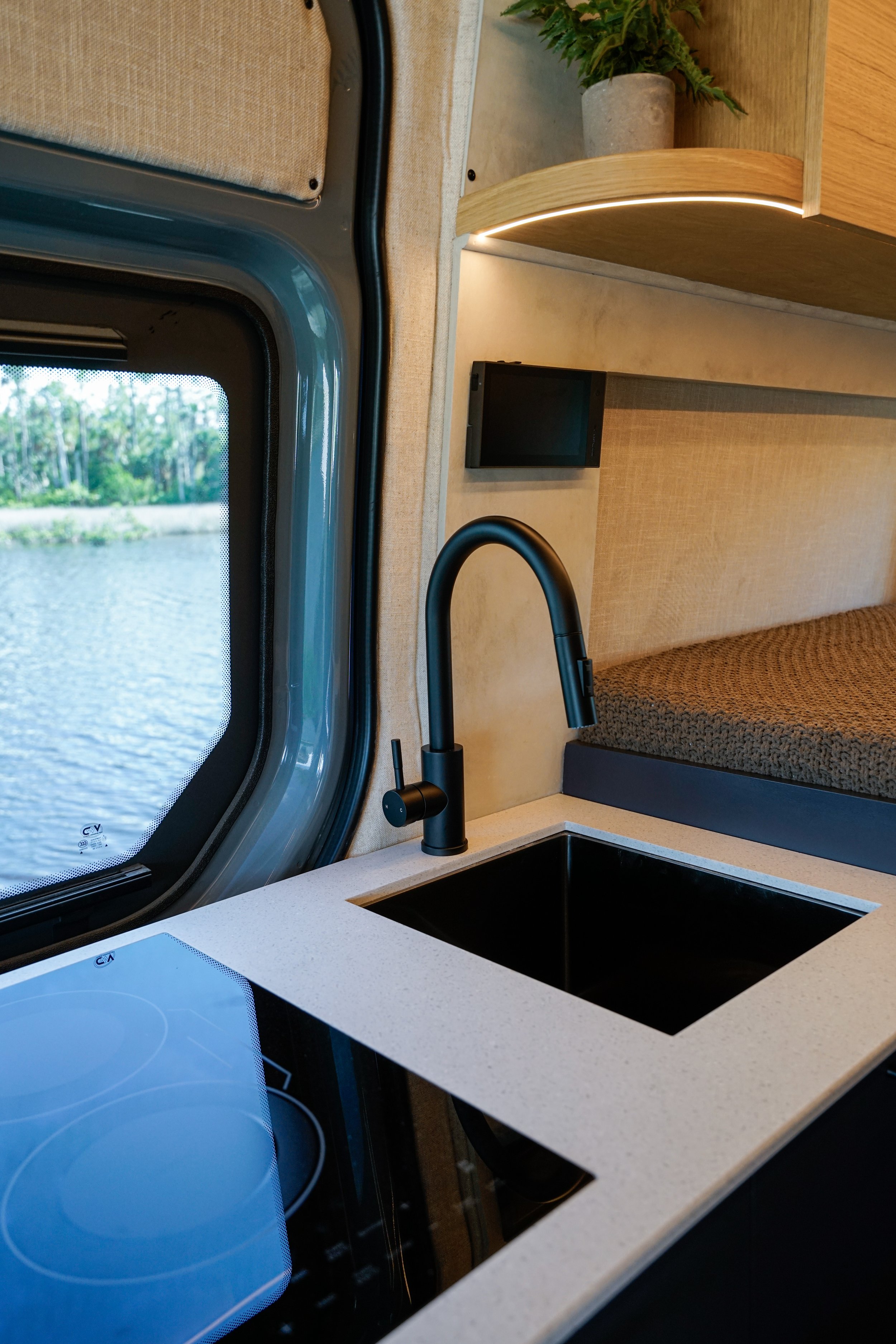 Kitchen with black sink, black faucet, white countertop, black electric stove, and window with outdoor view of green trees and water.