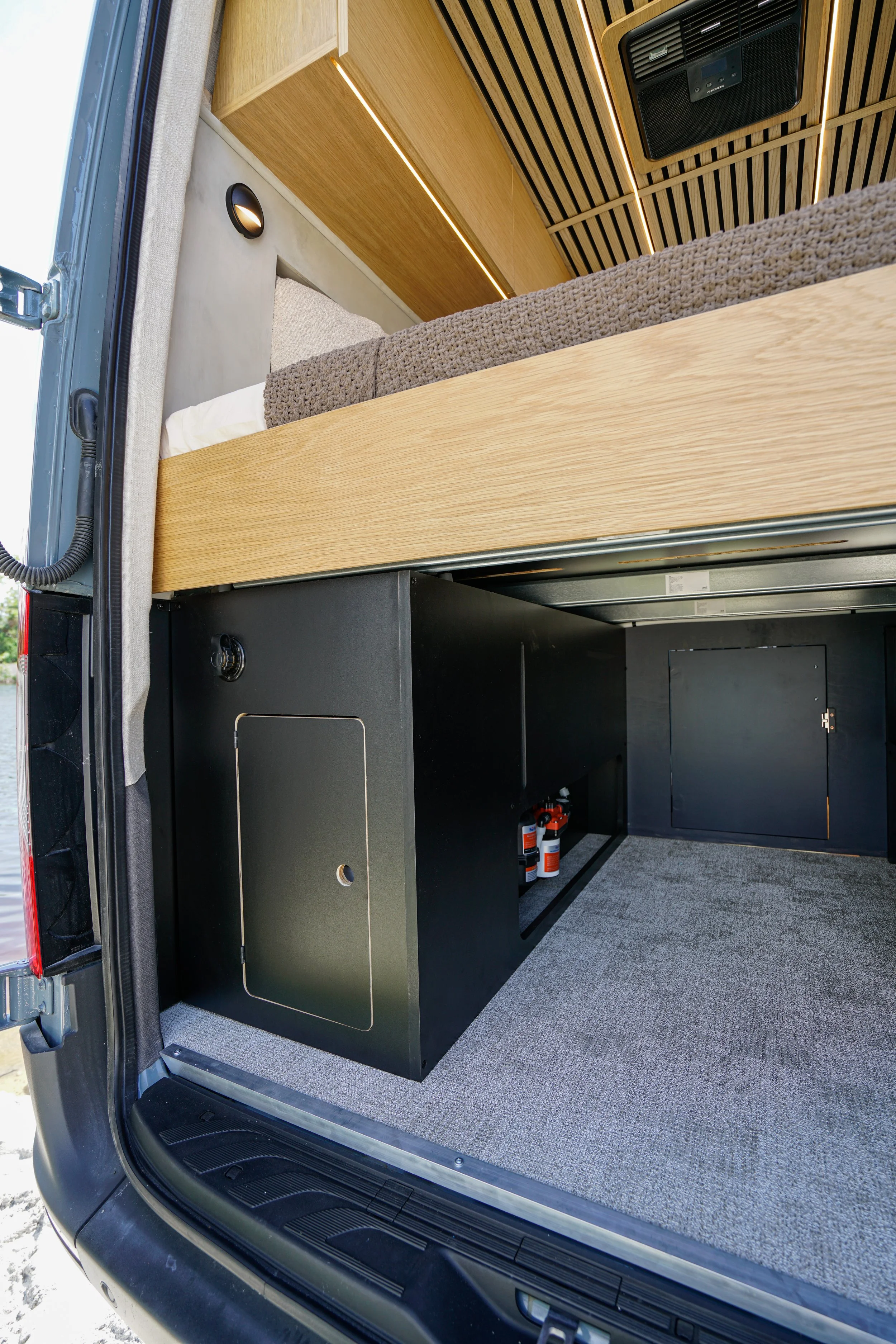 Inside a vehicle, showing a custom storage unit with  2TEC2 floor, and wooden paneling on the ceiling with LED lighting.