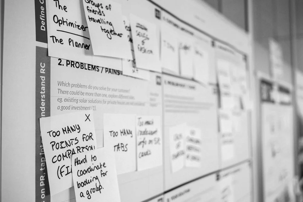 Whiteboard with numerous sticky notes and paper notes, some handwritten, related to problem-solving and group activities.