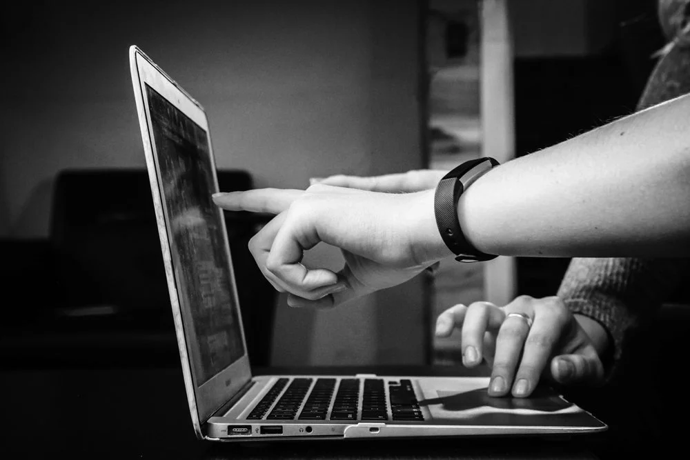 Person pointing at a laptop screen while another person watches.