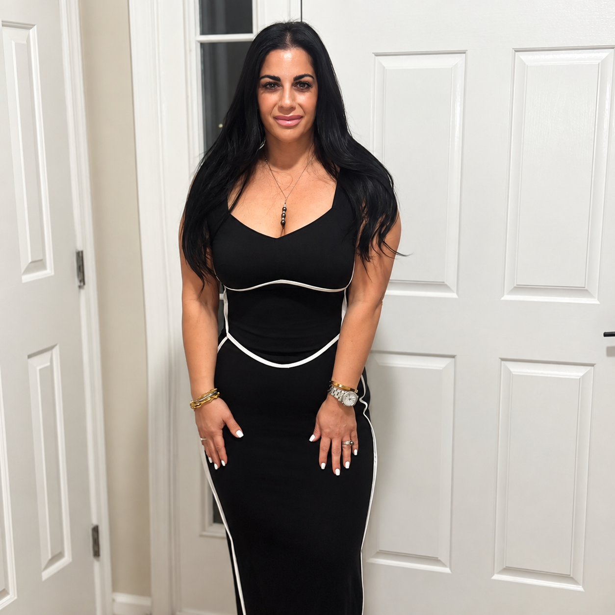 A woman with long dark hair in a black and white dress standing in front of white double doors.