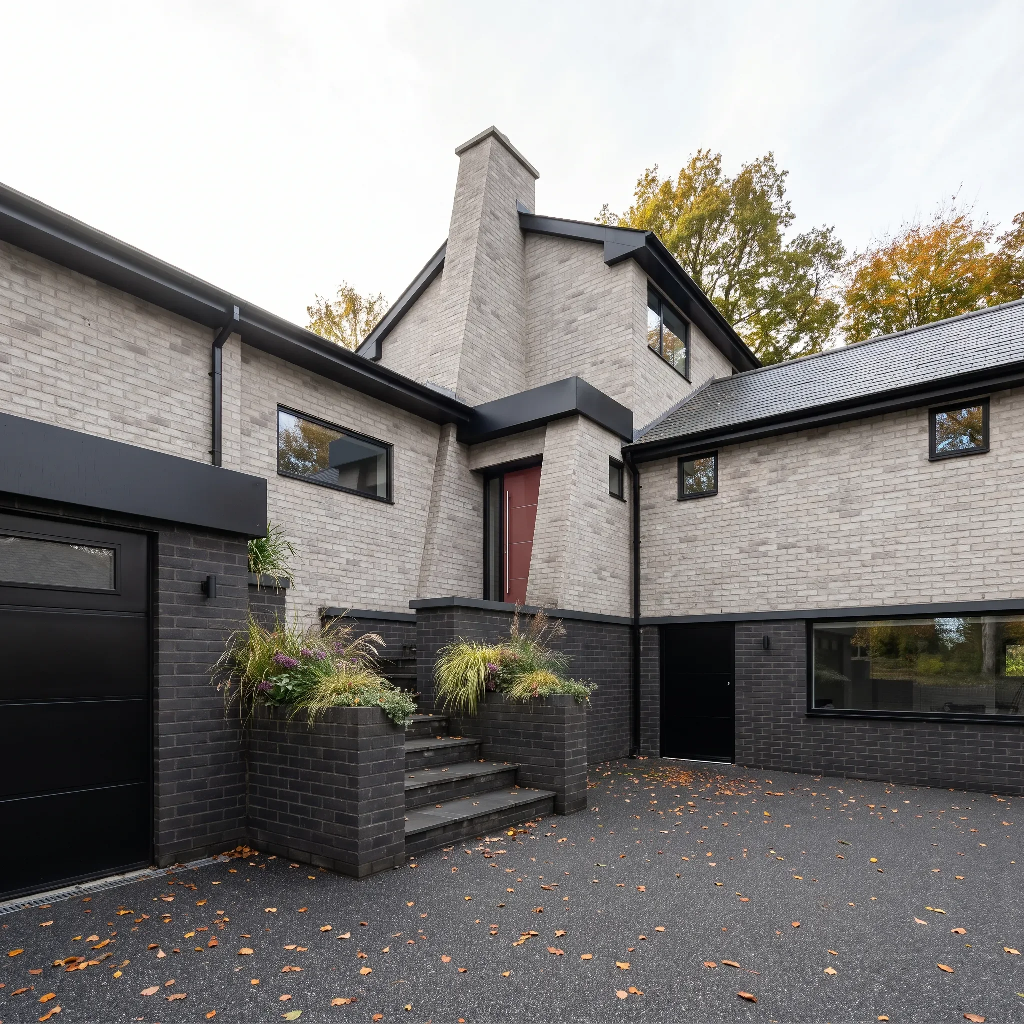A muted red entrance door brings colour to the pale brick and dark detailing