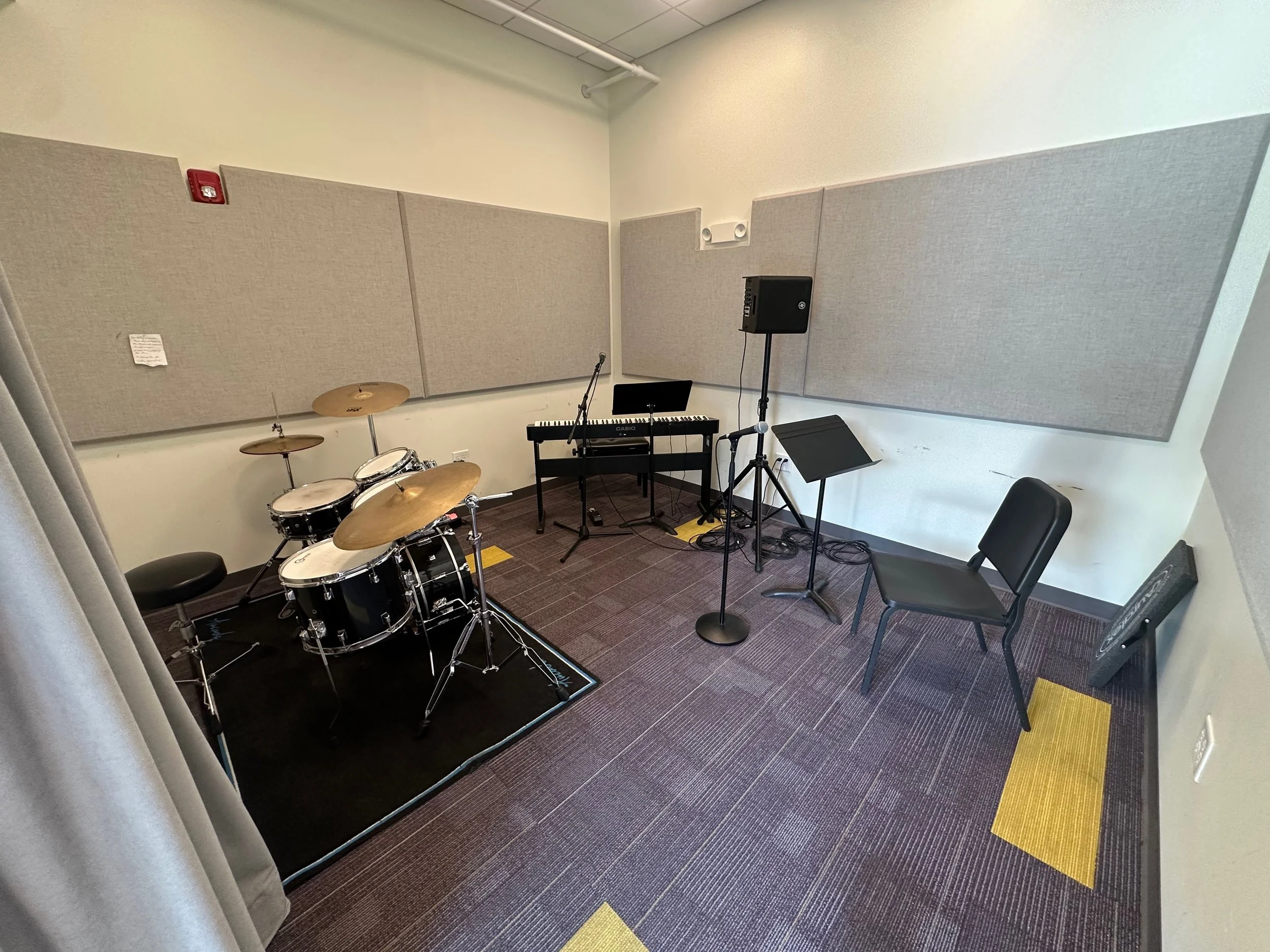 Music rehearsal room with drum set and digital piano, featuring soundproof panels on walls.