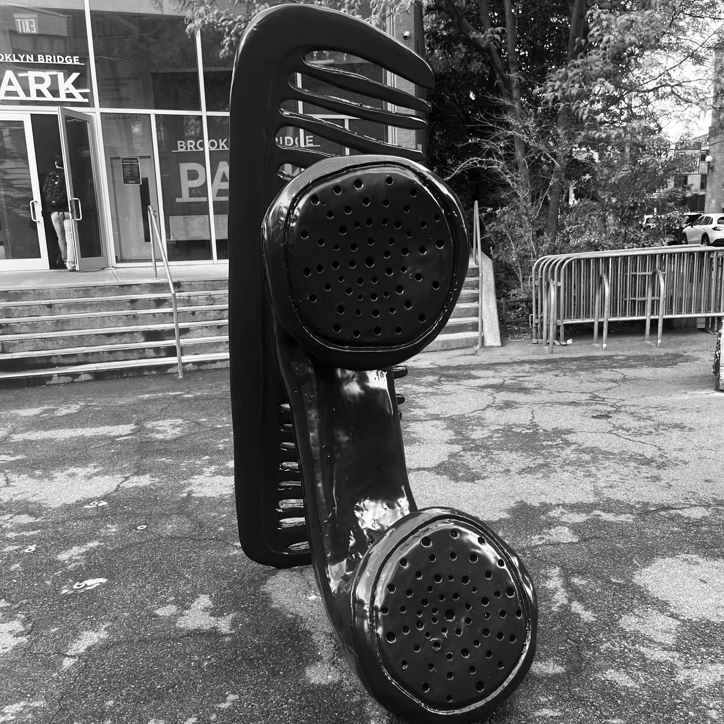 Black and white photograph of a public art sculpture of a telephone receiver and comb by artist Woody de Othello in Brooklyn Bridge Park