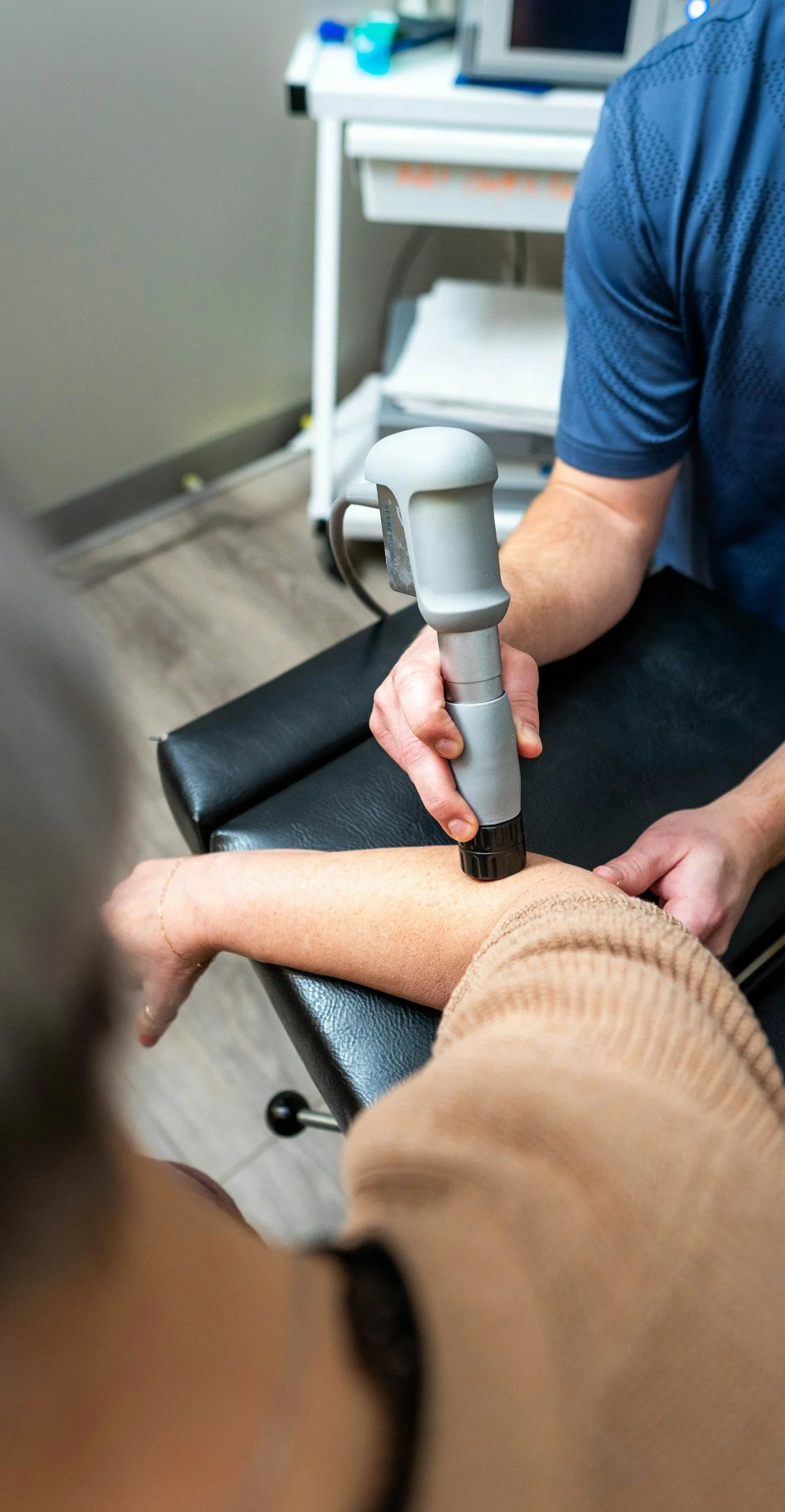 A healthcare professional uses an ultrasound device on a patient's forearm while sitting in a medical examination room.