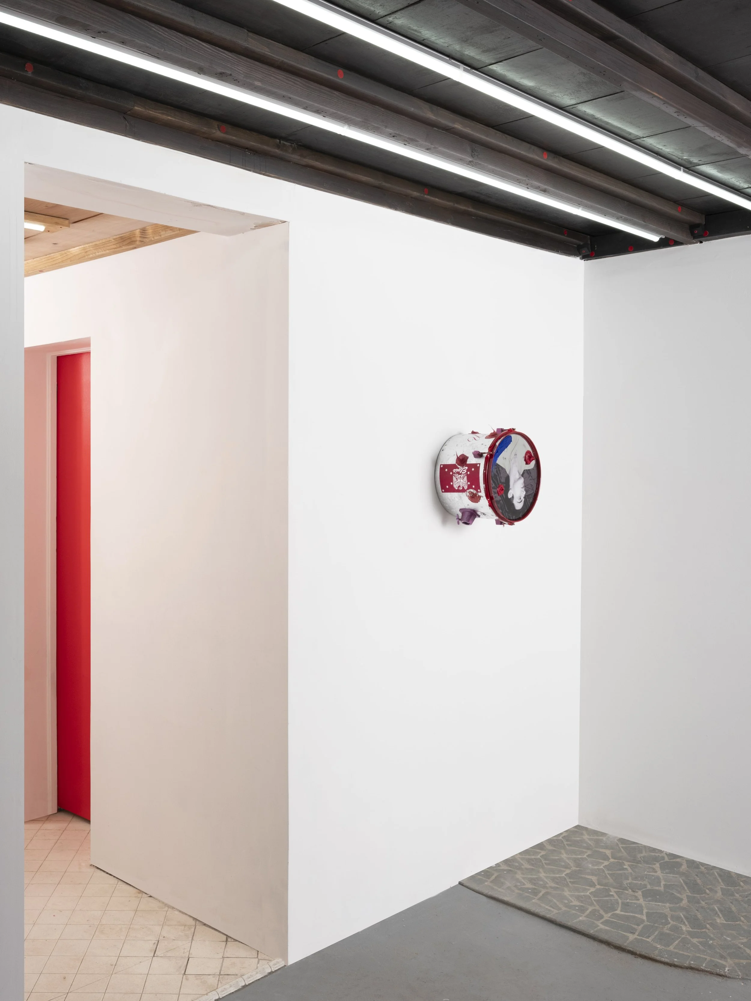 A white gallery wall with a fire alarm and a visible ceiling featuring black wooden beams and linear LED lights.
