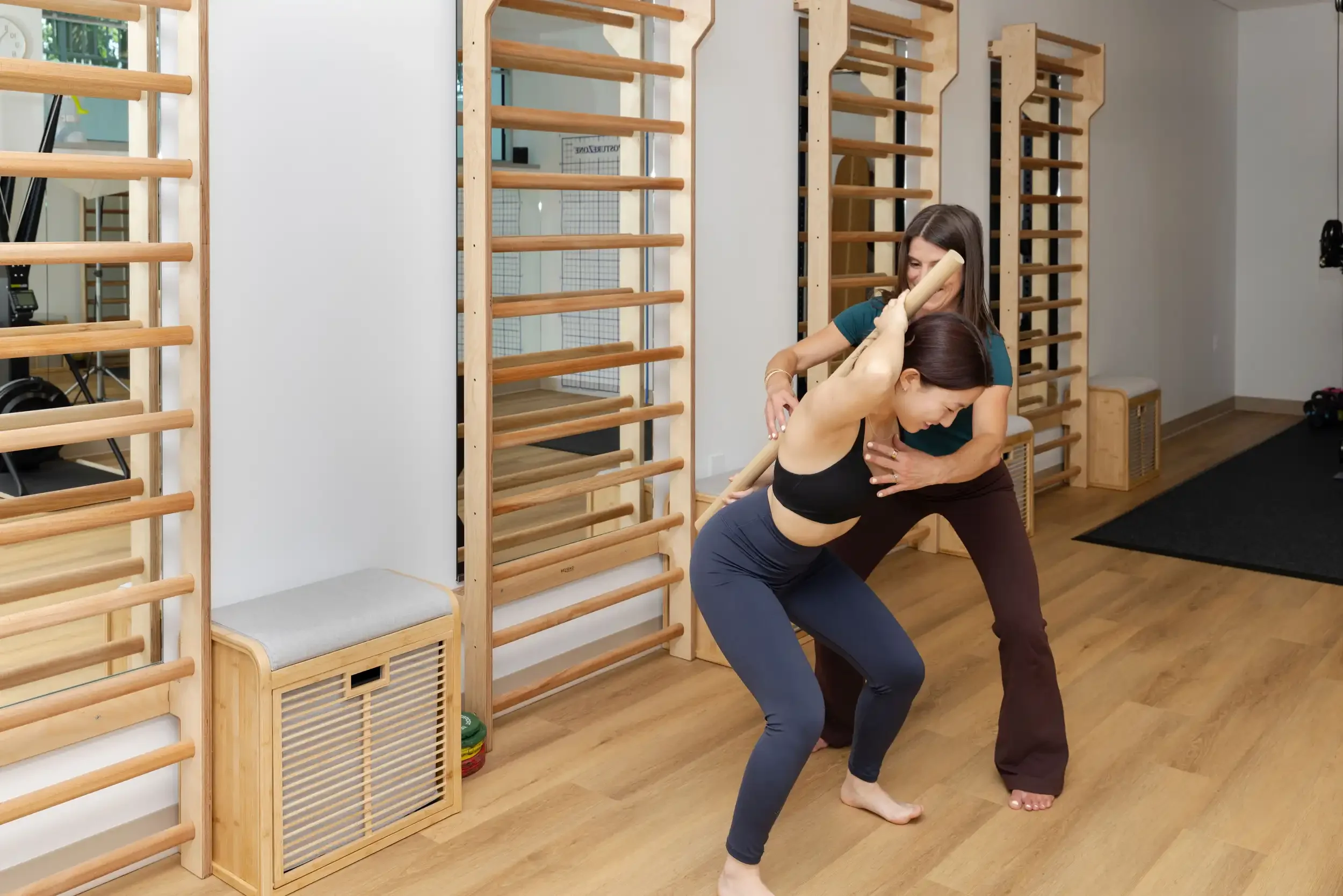 physical therapist guiding an adult patient in a squat Schroth exercise with a wooden bar