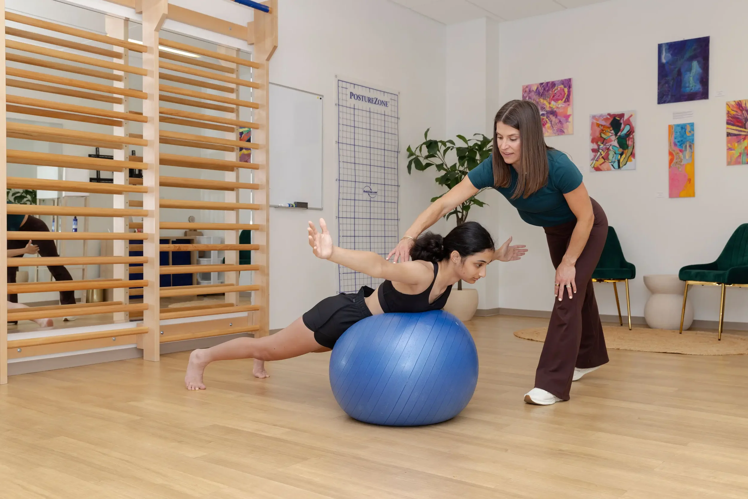 physical therapist guiding a teenage patient in a Schroth exercise on a blue exercise ball, with her arms extended to the sides