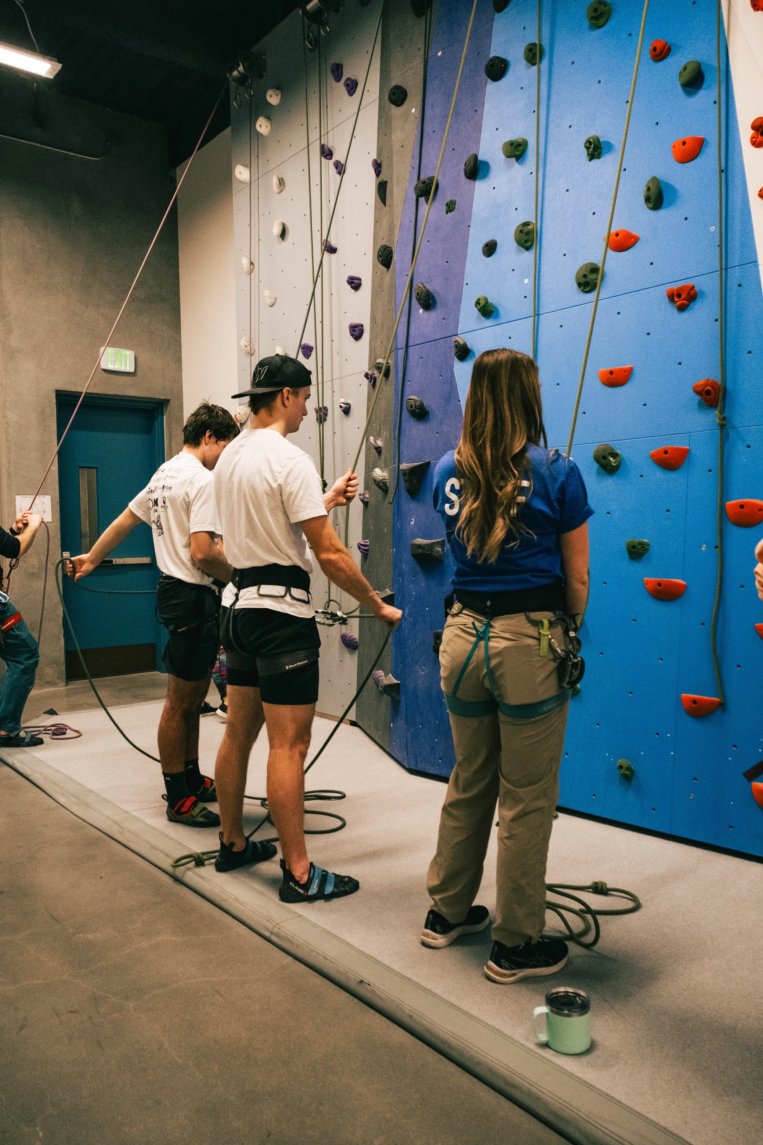 Staff member is instructing a class to learn how to belay and use ropes for climbing.