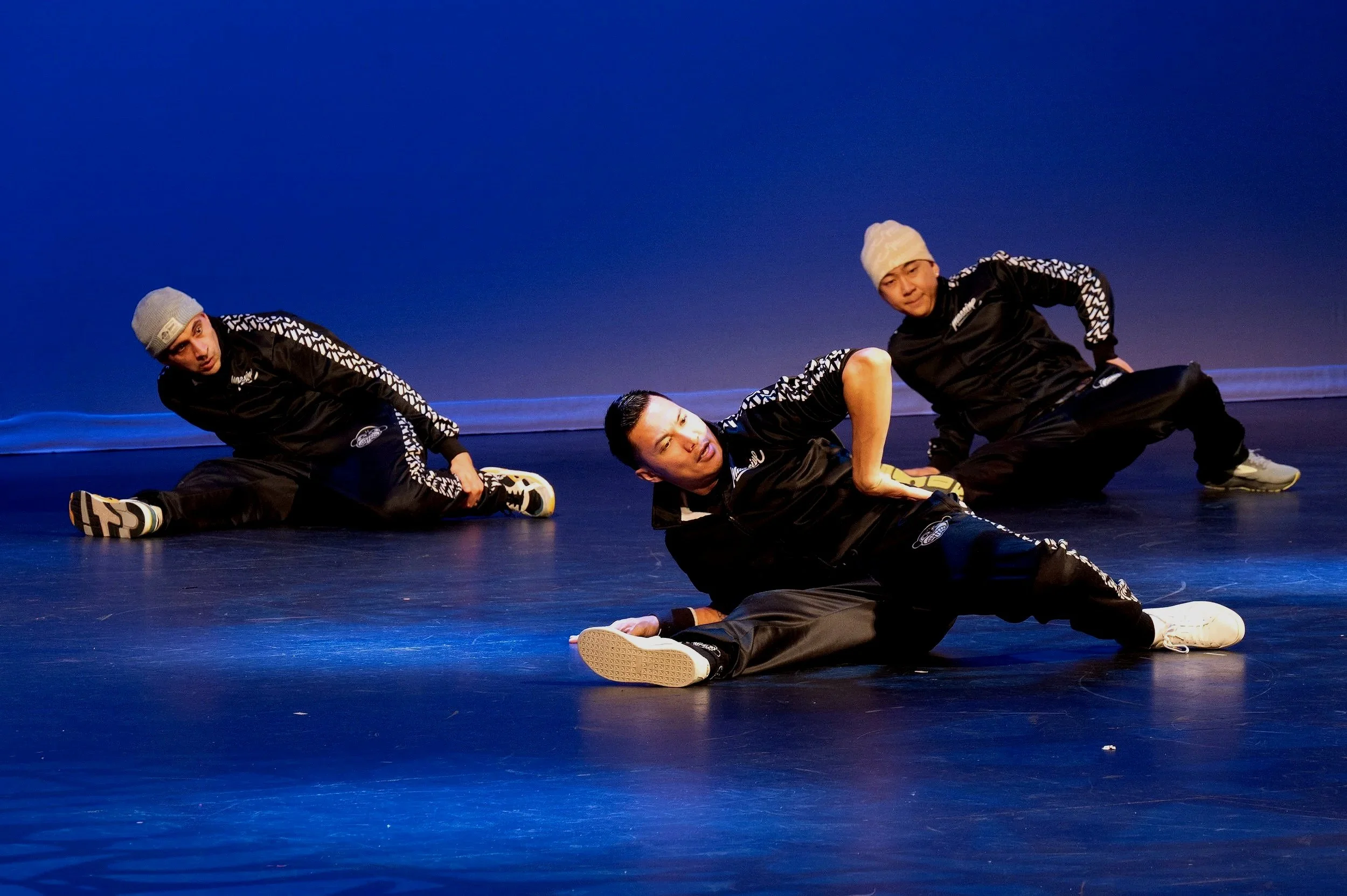 Three breakdancers from the Massive Monkees crew performing on stage during a Lunar New Year celebration, mid-move under stage lighting.