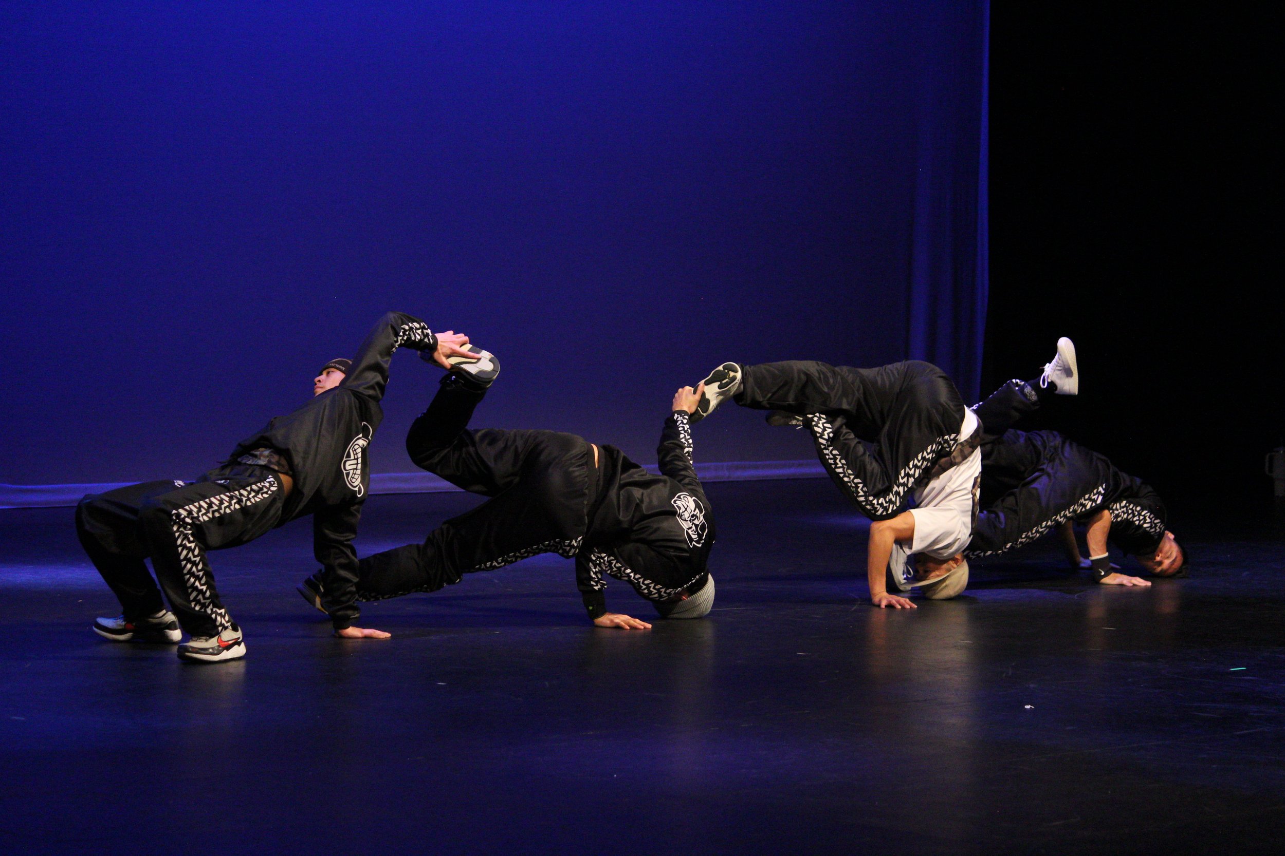 Four breakdancers from the Massive Monkees crew performing a group move on stage during a Lunar New Year celebration.