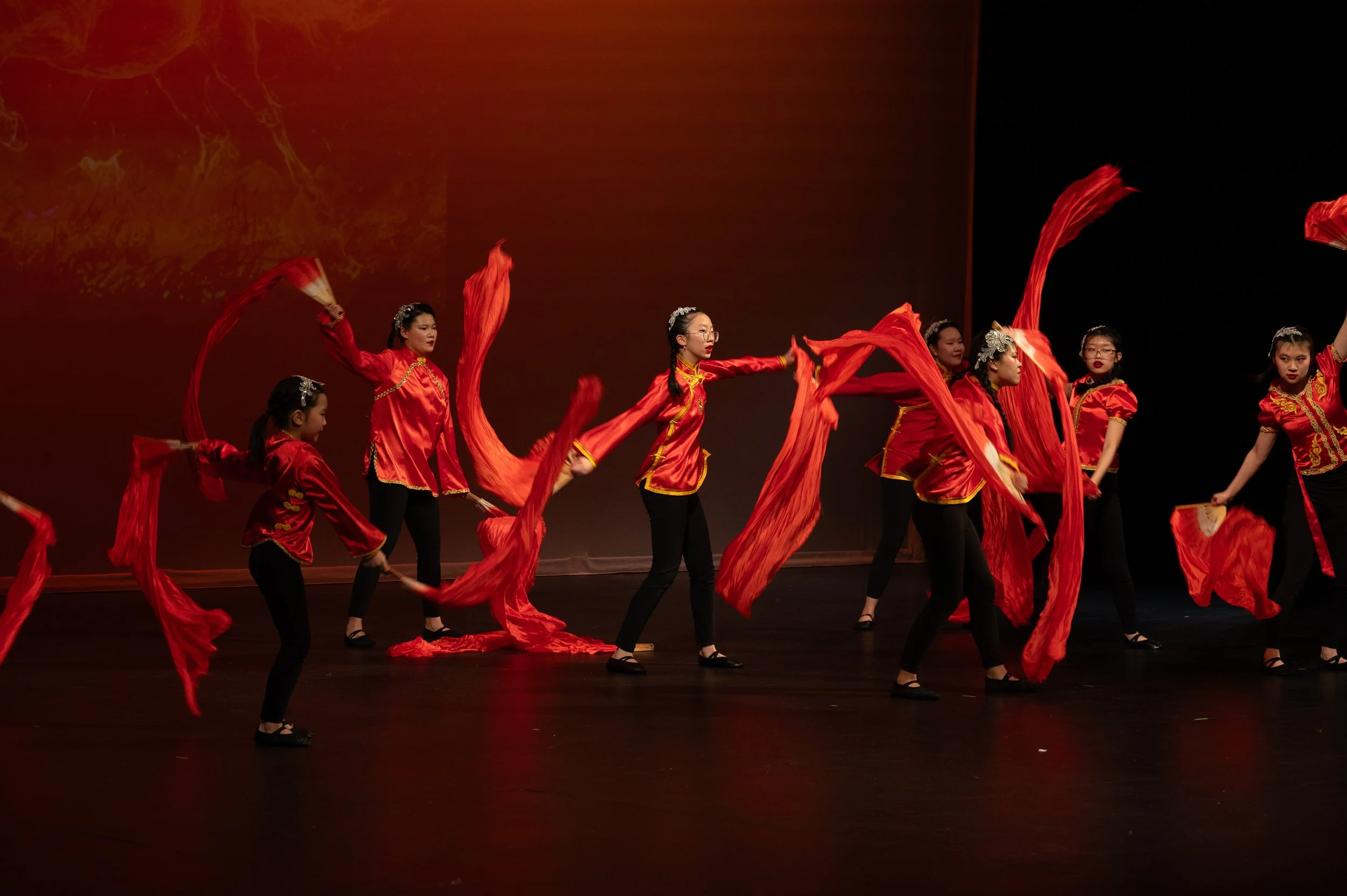 A group of younger dancers from the Melody Dance Institute performing a fire themed ribbon dance on the stage
