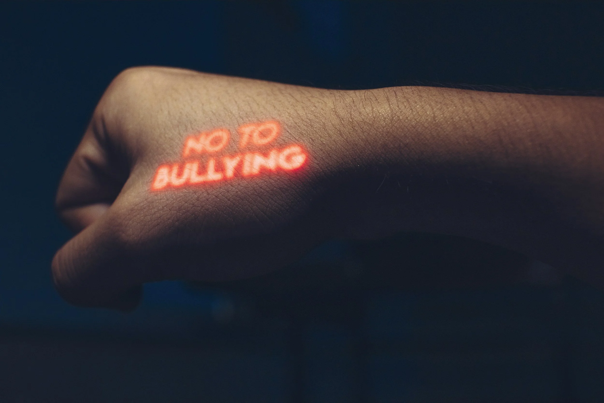 A person's hand with a 3D laser projection displaying the words 'NO BULLYING' in red on the back of the hand.