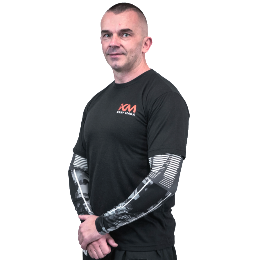 A man with short hair and light skin, wearing a black T-shirt with red and white logo, standing with arms crossed against a white background.