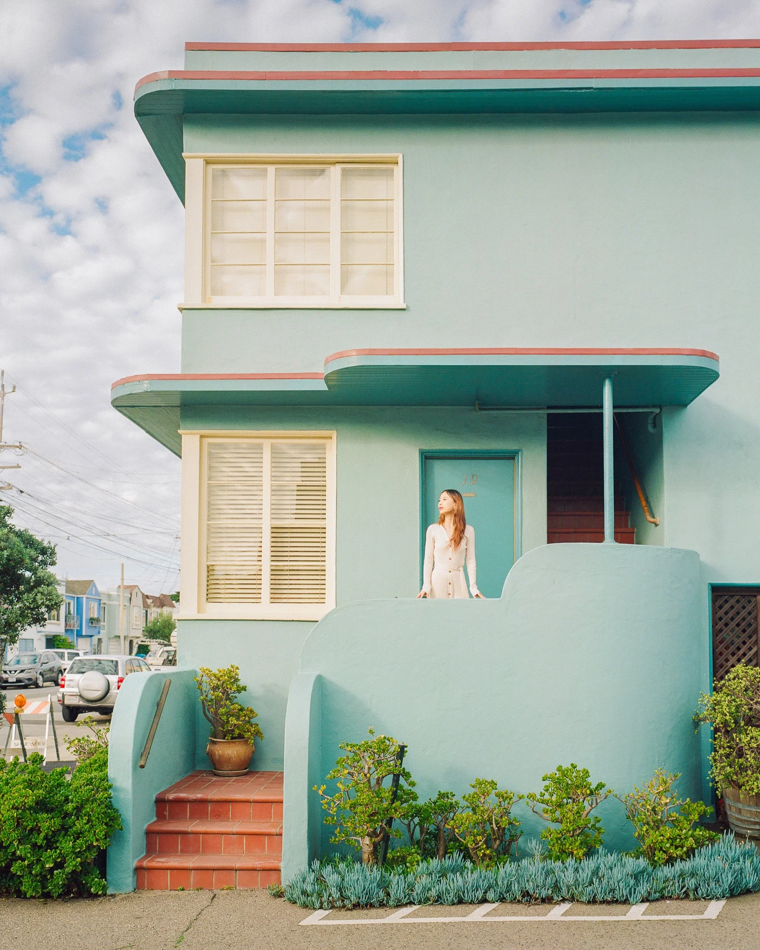 Woman in a white dress standing outside a mint-green Art Deco house