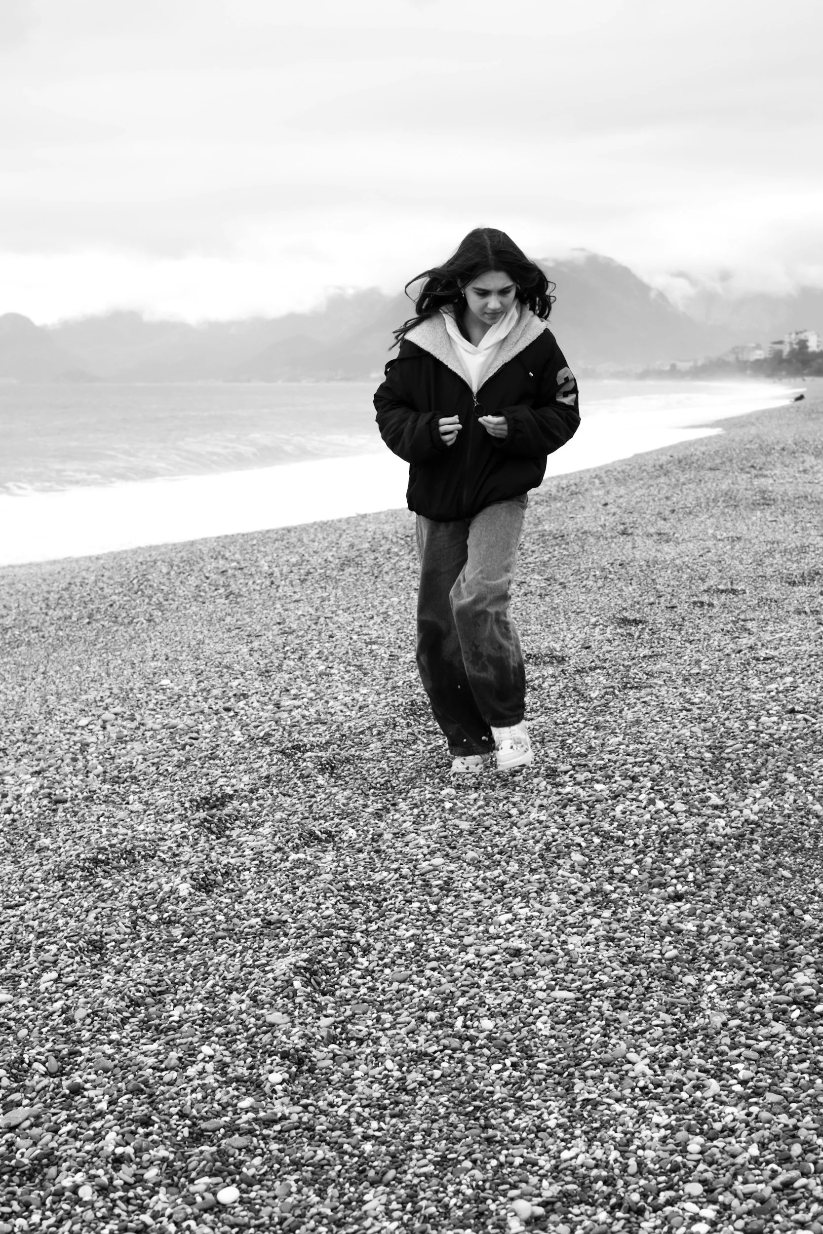 A young woman walking on a pebble beach with mountains and cloudy sky in the background