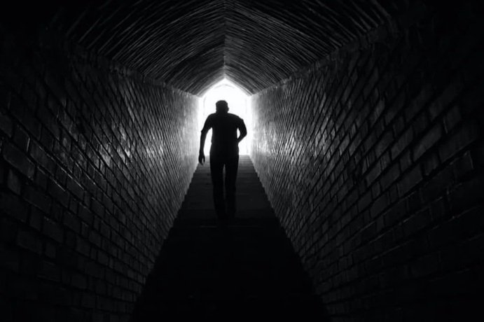 Silhouette of a person walking through a dark, tunnel-like passageway with light at the end.
